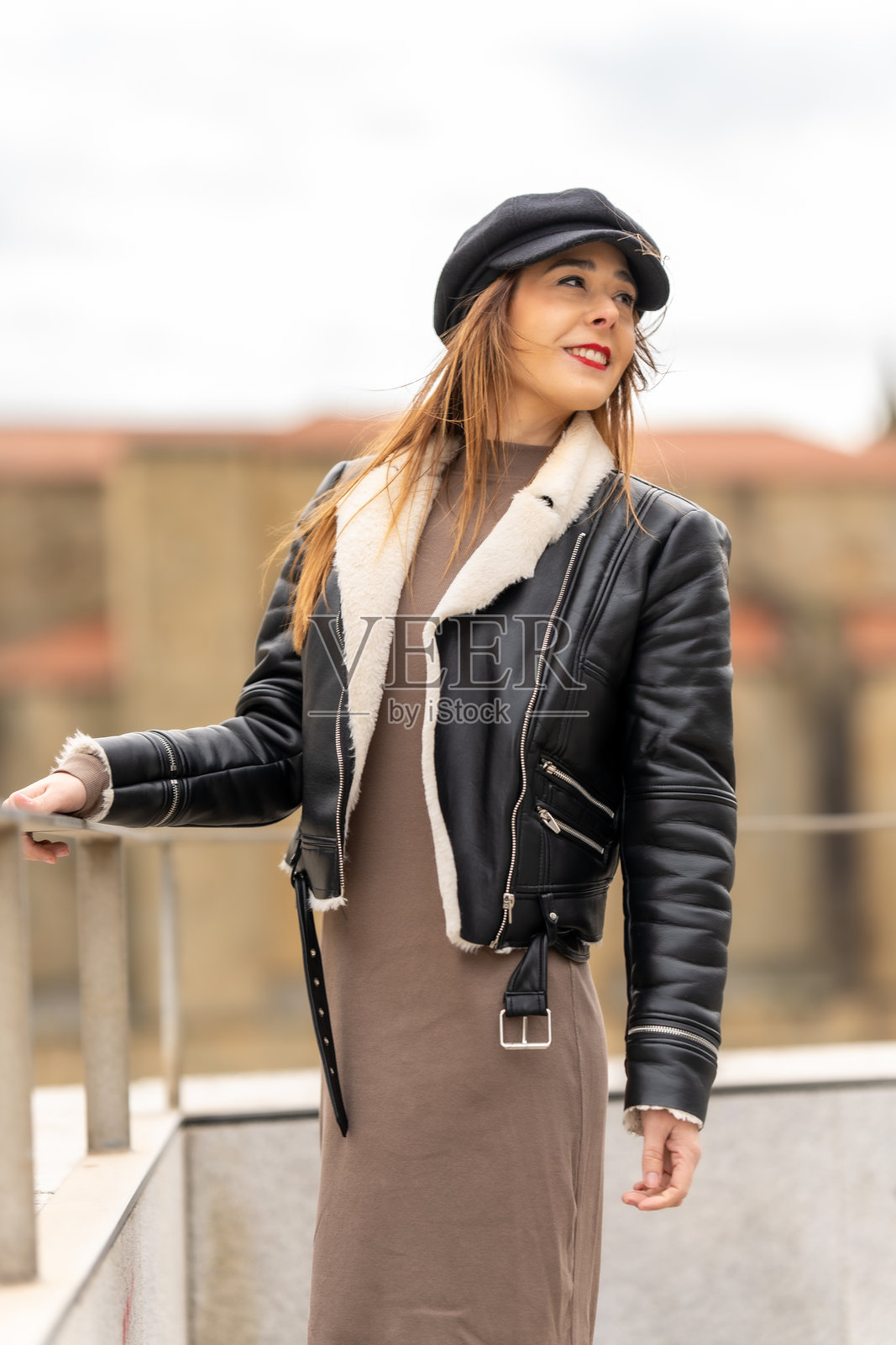 时尚年轻女性在阳台上摆姿势，穿着时尚的黑色夹克和报童帽照片摄影图片