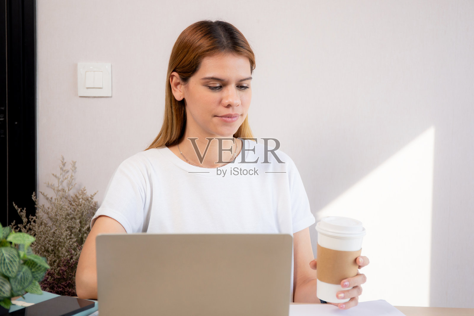 快乐的年轻白人女商人在家办公室喝咖啡，同时使用笔记本电脑工作，快乐的女商人在放松时喝饮料，商业概念。照片摄影图片