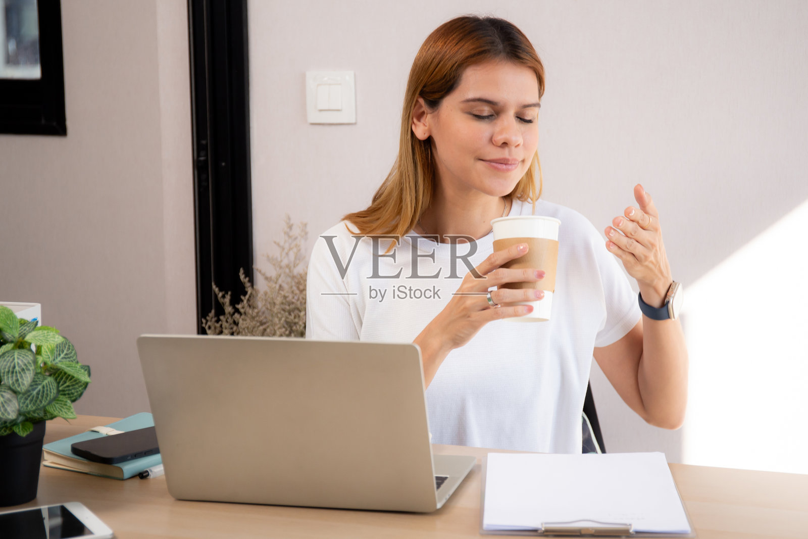 快乐的年轻白人女商人在家办公室喝咖啡，同时使用笔记本电脑工作，开心的女商人在放松时喝饮料，商业概念。照片摄影图片