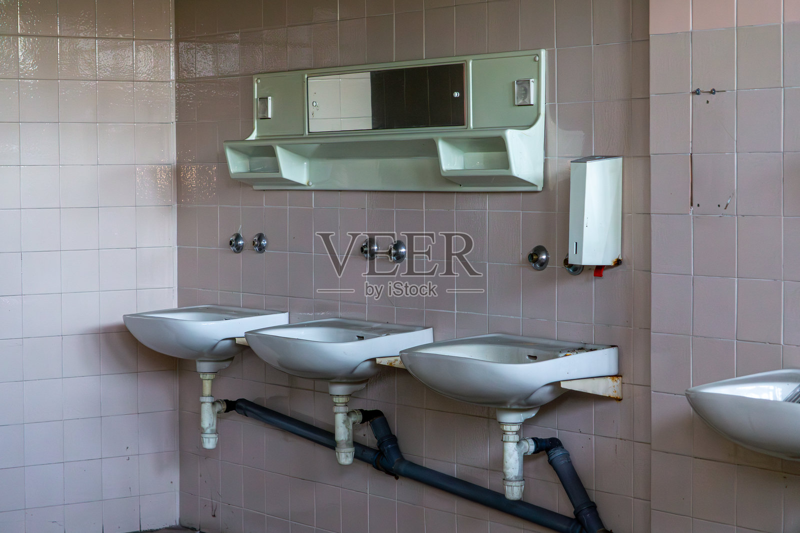 破旧不堪且不完整的工厂厕所，洗手池和架子位于一座废弃的生产厂房内。管道连接。照片摄影图片