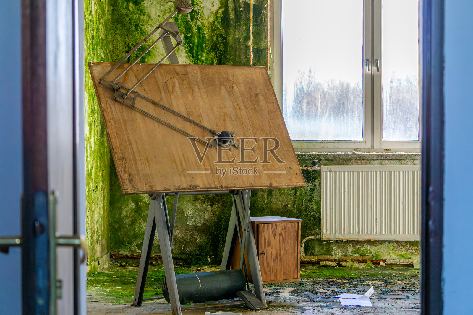 旧历史绘图桌，项目用绘图板。肮脏、发霉、长满苔藓的墙壁。墙壁上的油漆和灰泥剥落，旧废弃生产厂房内湿度极高。照片摄影图片