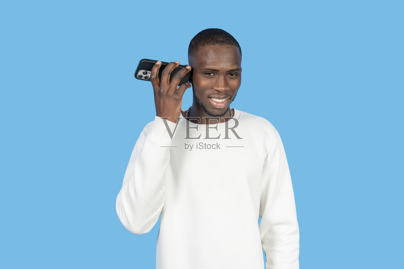 年轻男子在蓝色背景下用智能手机听音乐照片摄影图片