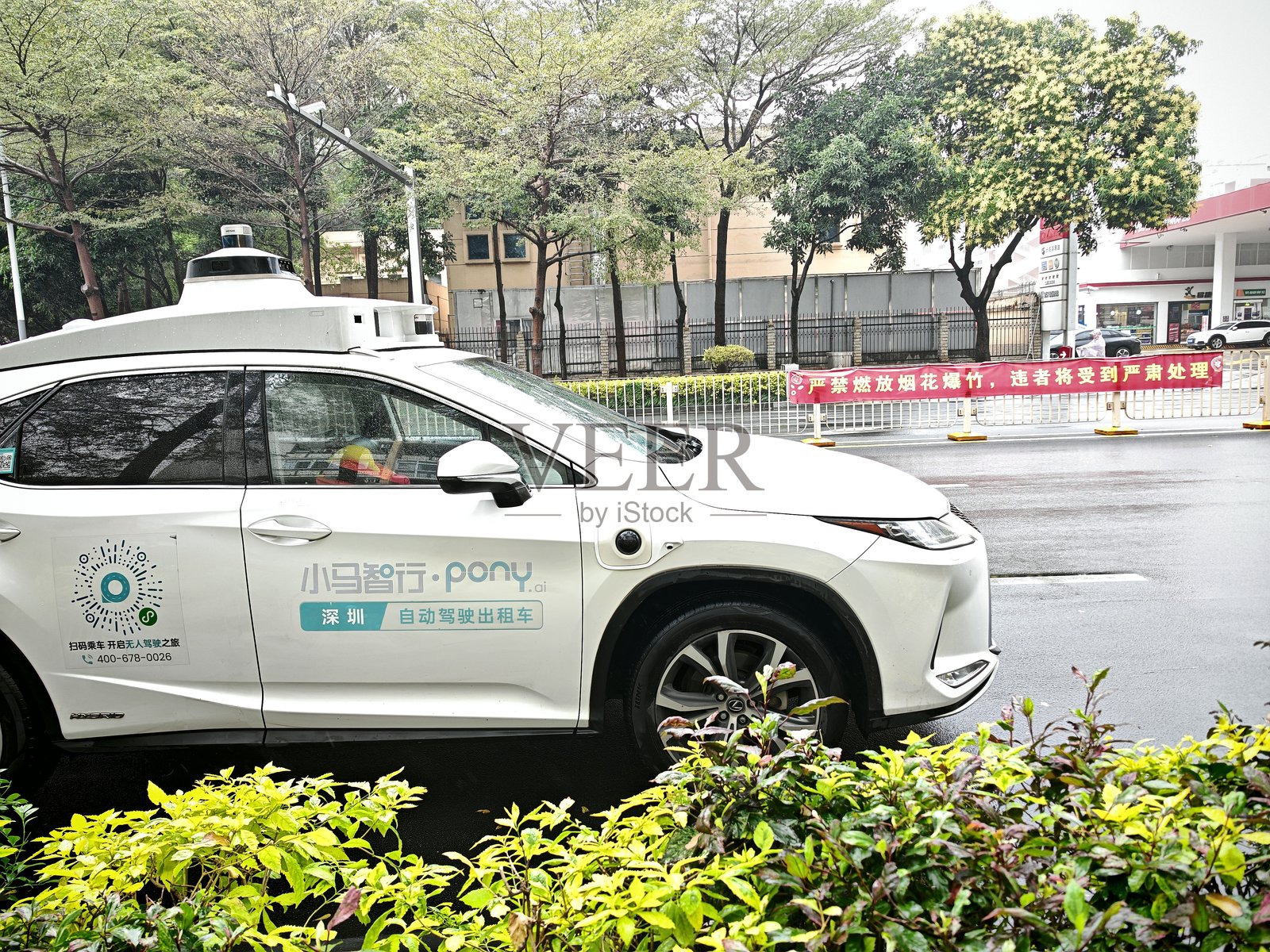 配备激光雷达和传感器的自主白色汽车停在道路上，背景是绿色的树木、灌木和城市建筑。照片摄影图片