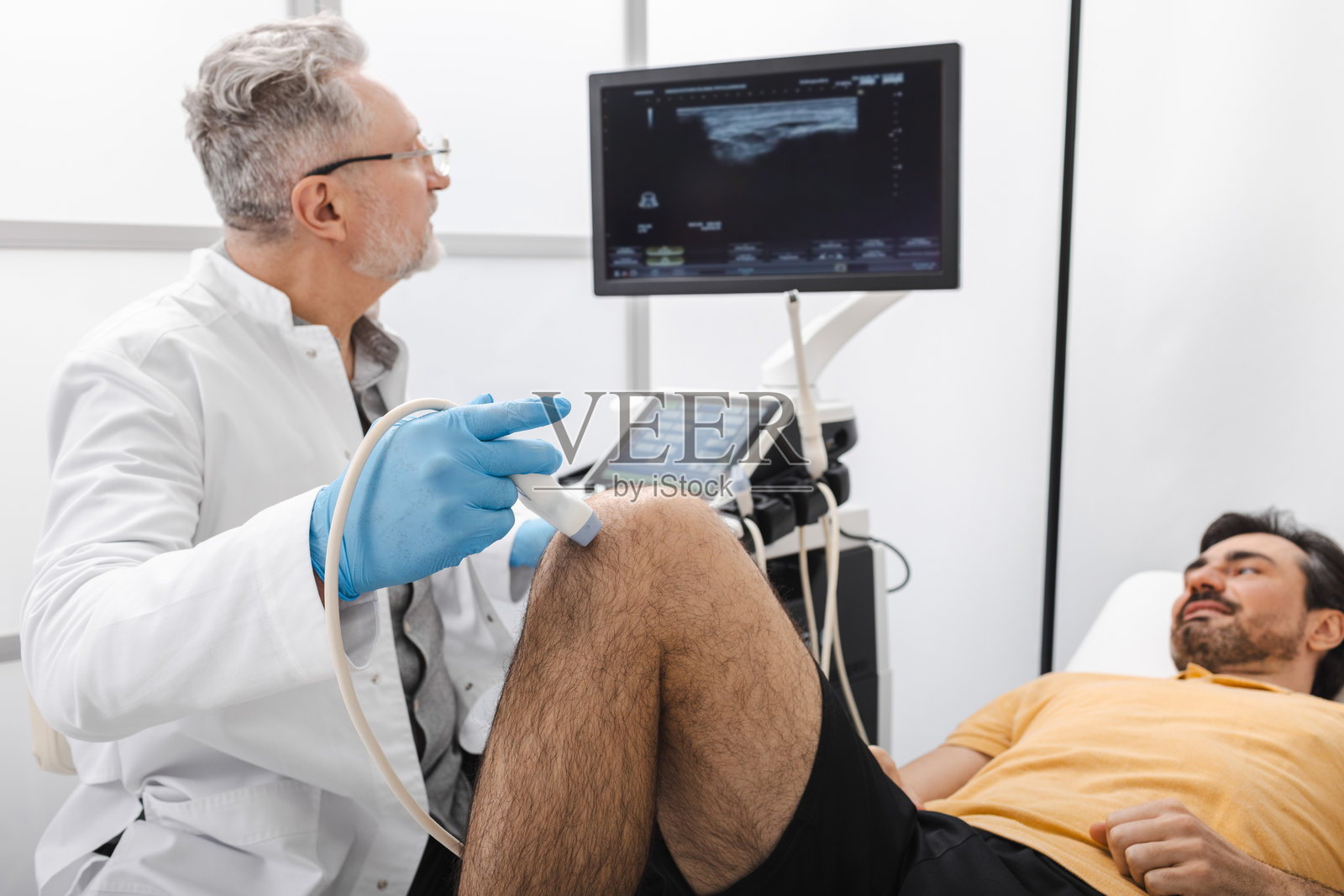 运动员膝盖的超声检查。经验丰富的超声医生在受伤后检查运动员的膝盖。照片摄影图片