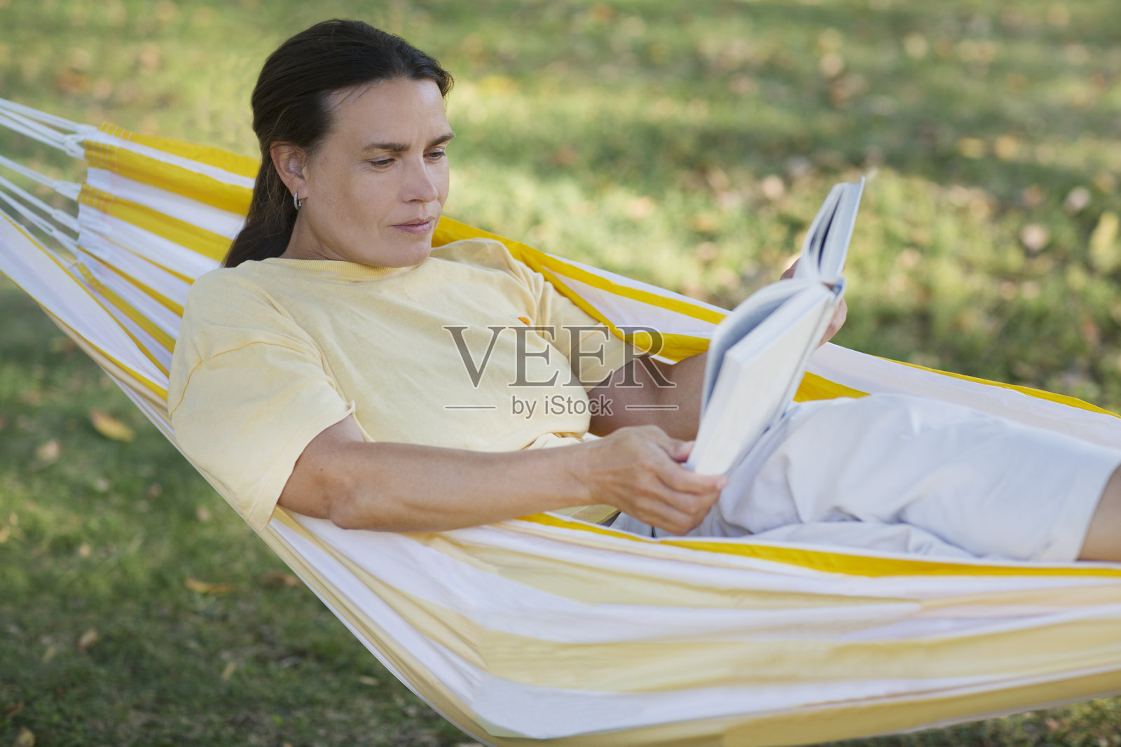 慢生活。享受生活中的小事。中年女性在夏季公园或花园的吊床上休息并阅读一本书的生活方式肖像。照片摄影图片