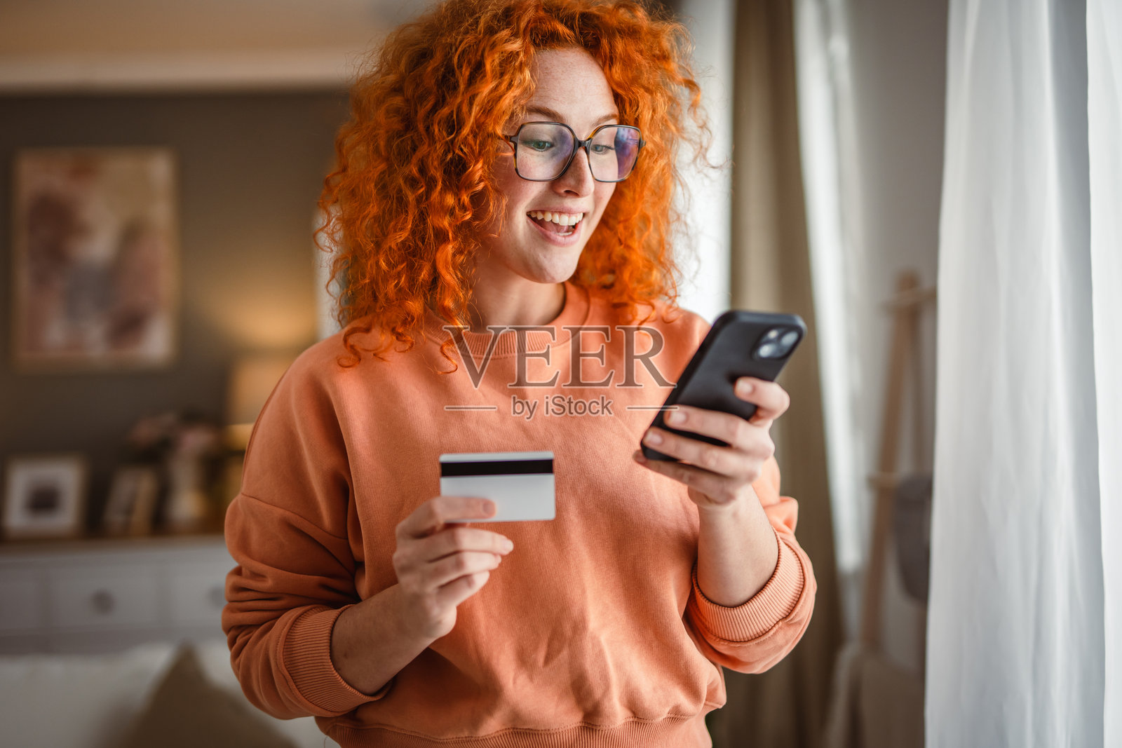 微笑的红发女性使用手机和信用卡进行支付照片摄影图片