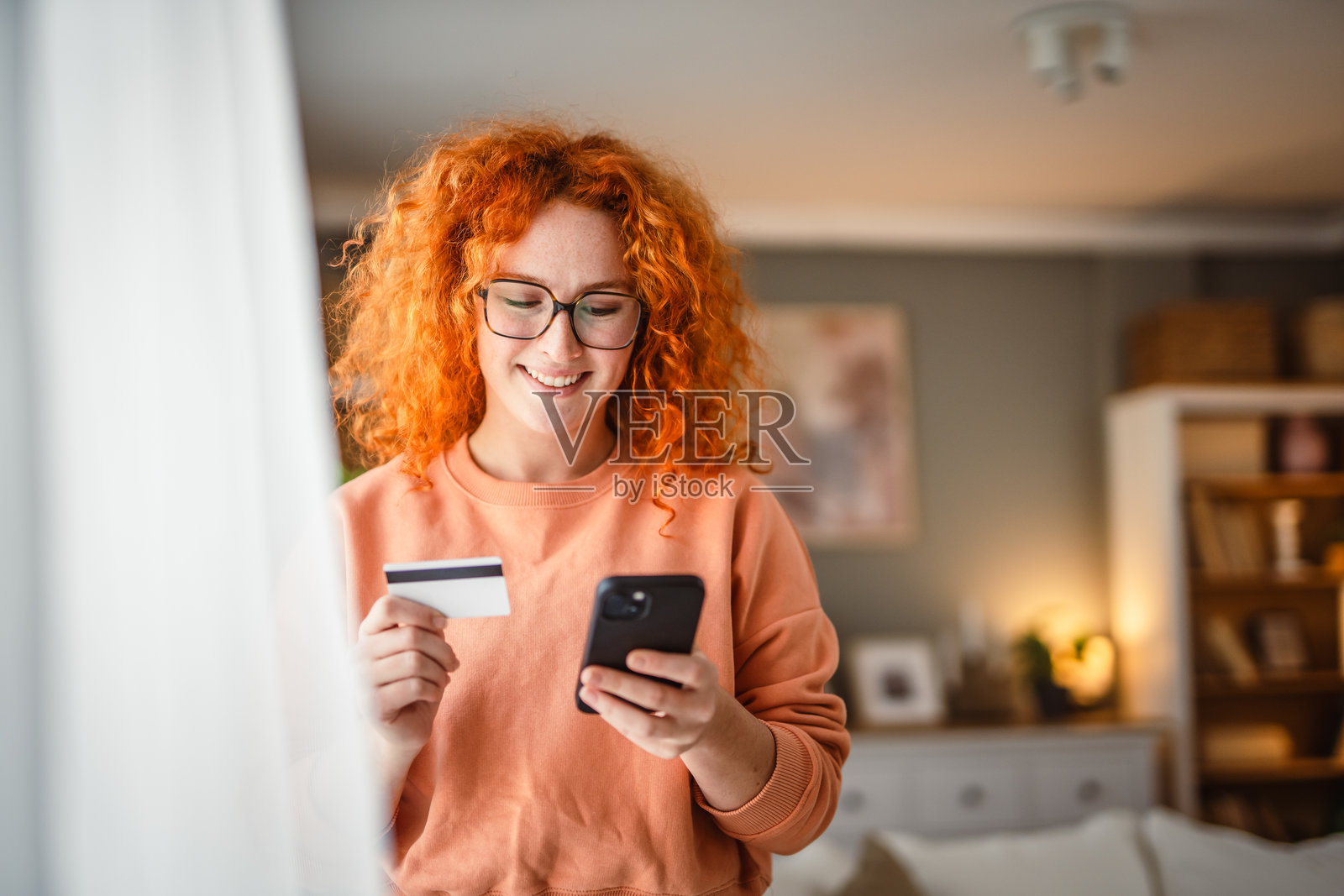 微笑的红发女性使用手机和信用卡进行支付照片摄影图片