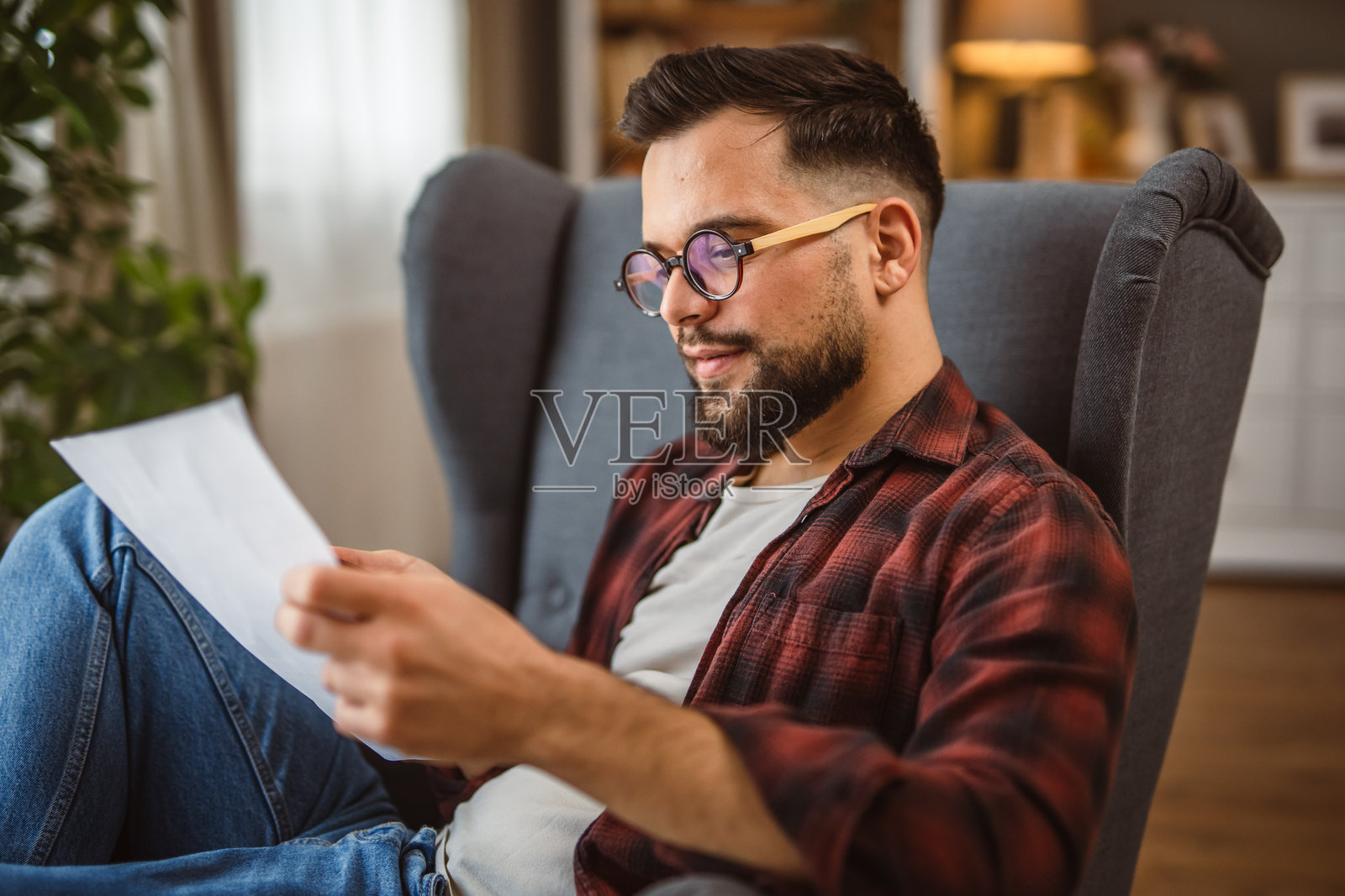 成年男子坐在扶手椅上，使用手机并阅读文件。照片摄影图片