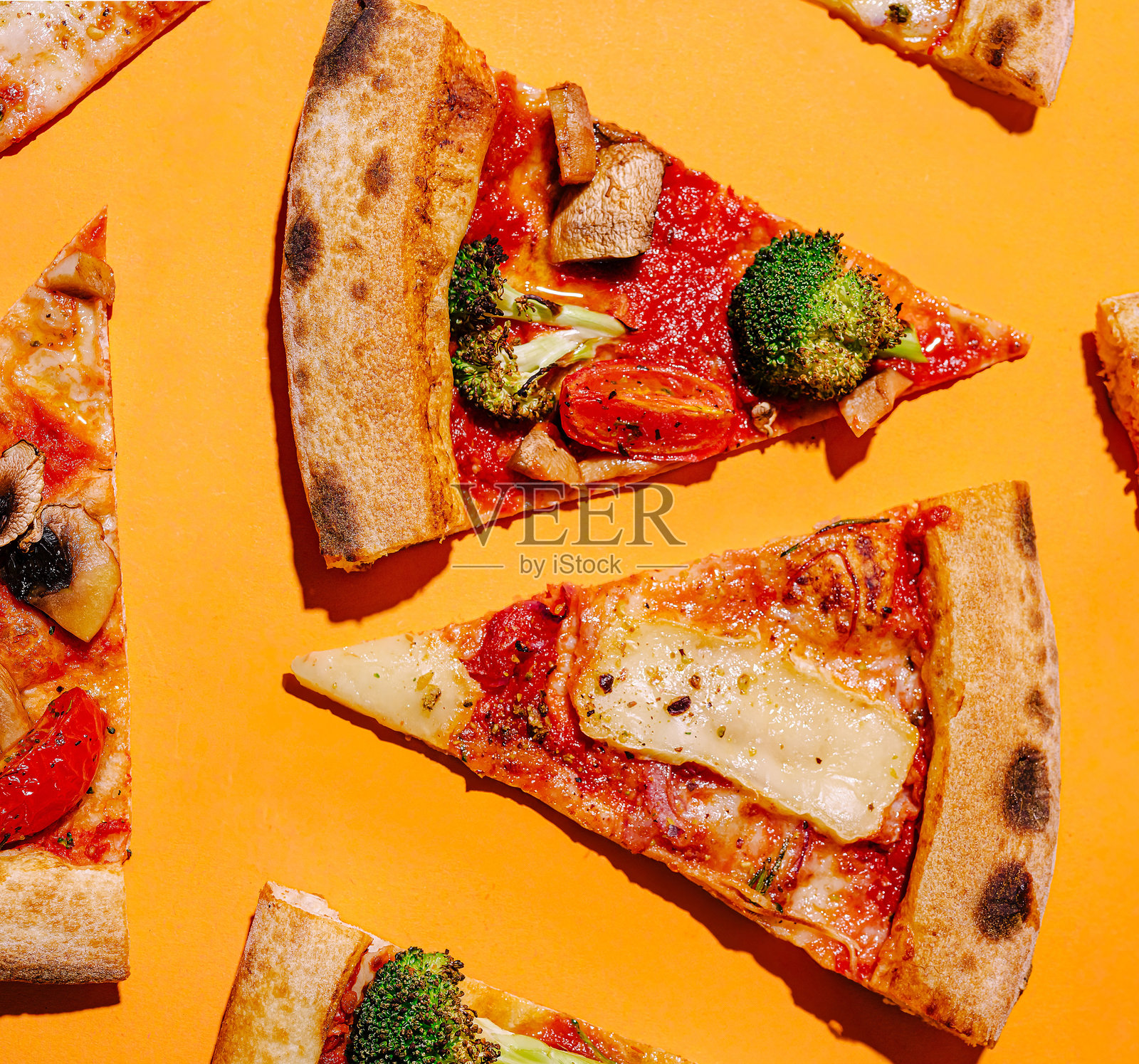 五彩缤纷的披萨片与蔬菜摆放在鲜艳的橙色背景上照片摄影图片