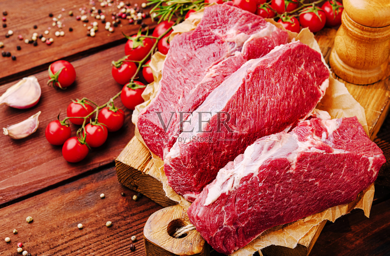 新鲜的牛肉切块放在木板上，旁边有香草和大蒜，背景是乡村风格的厨房环境照片摄影图片