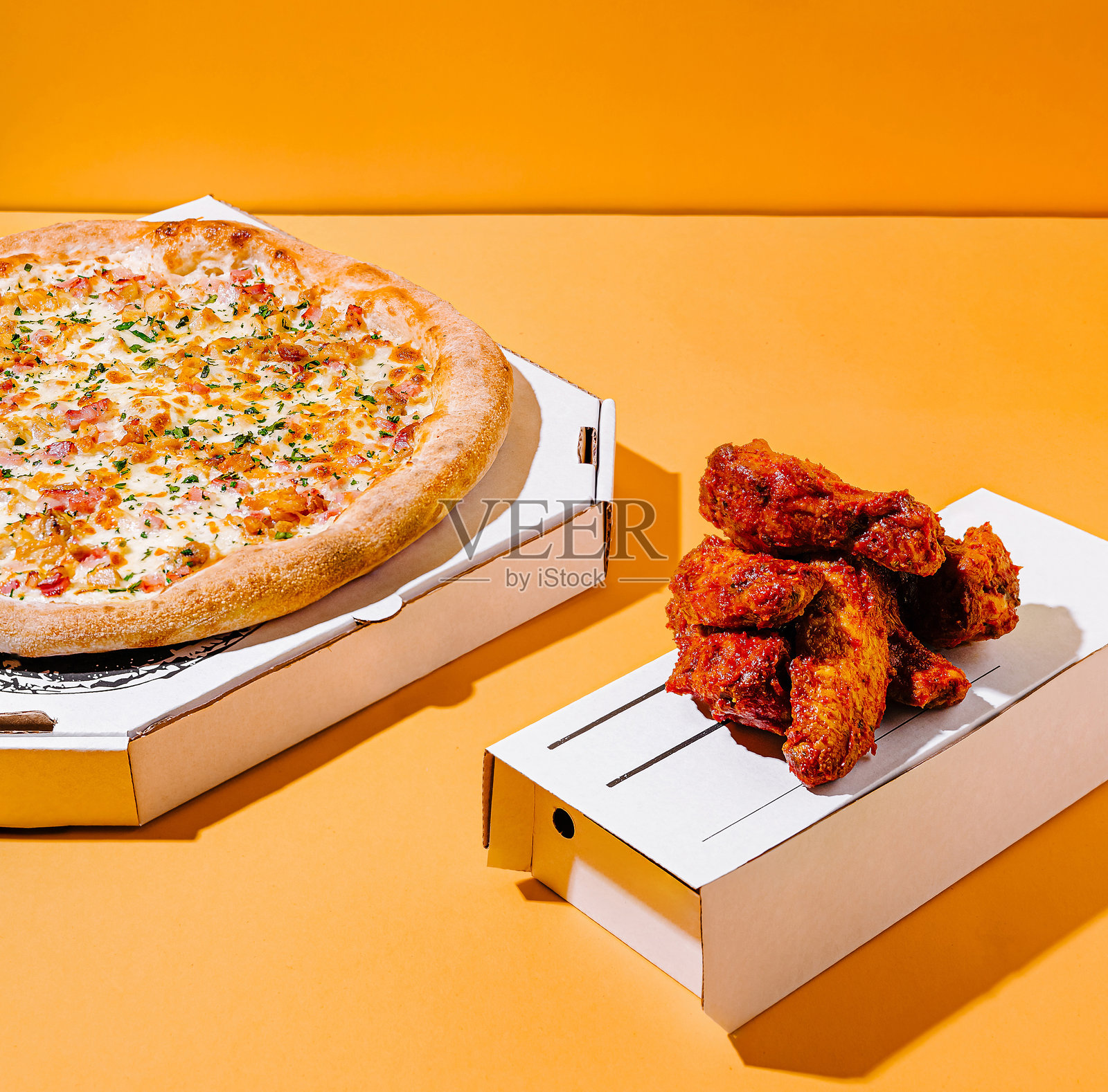 美味的比萨饼搭配酥脆的鸡翅，背景为鲜艳的橙色照片摄影图片
