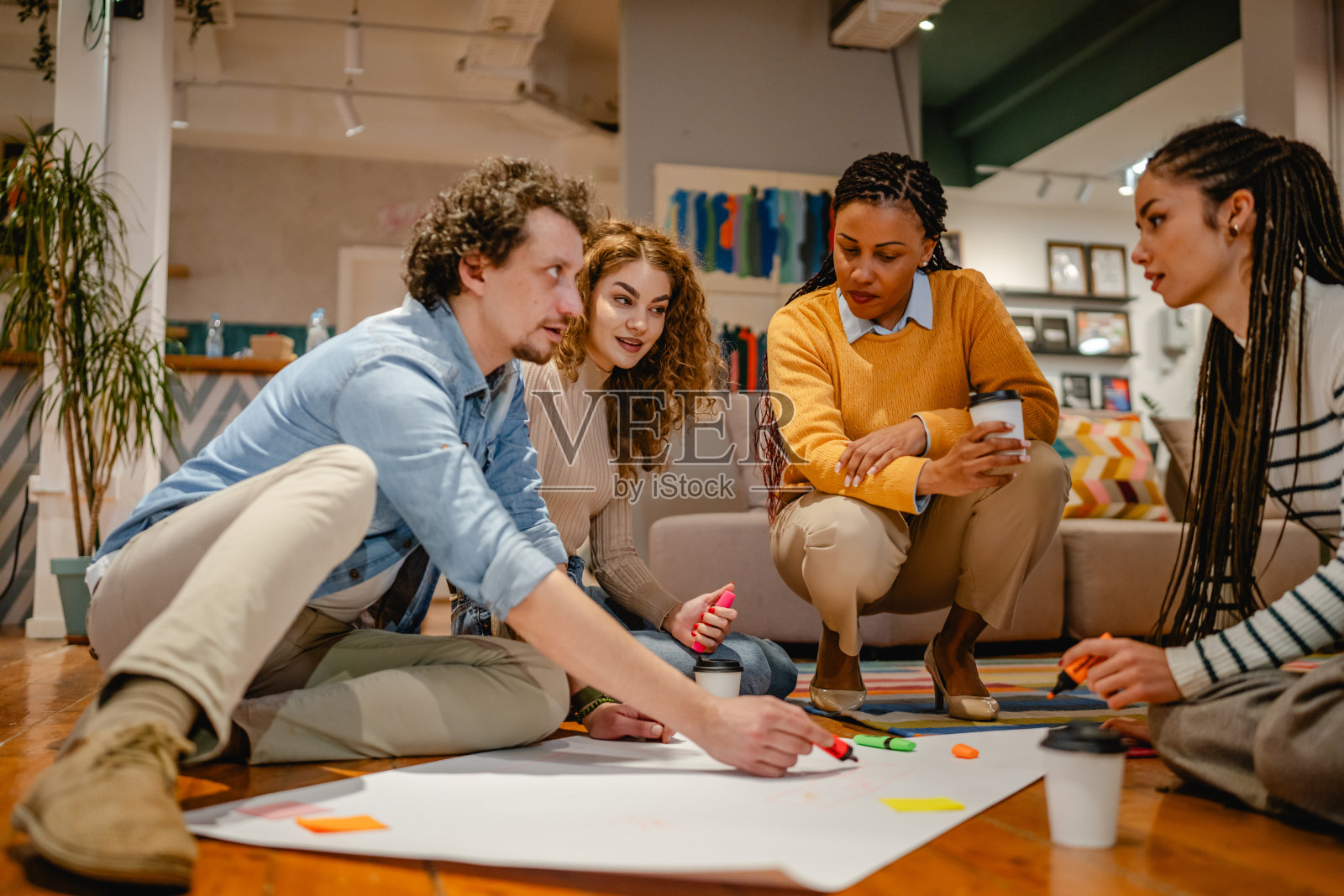 多元文化的同事们围坐在木地板上的一张大纸旁照片摄影图片