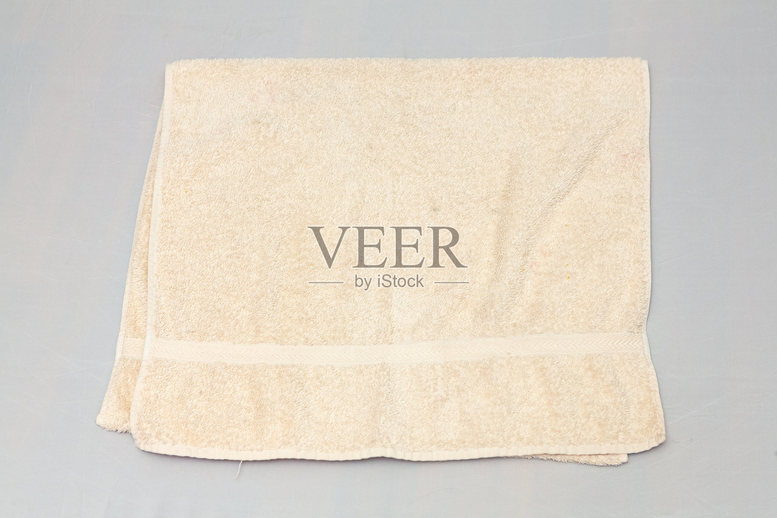 折叠的米色毛巾放在灰色背景上，象征着卫生与舒适。照片摄影图片