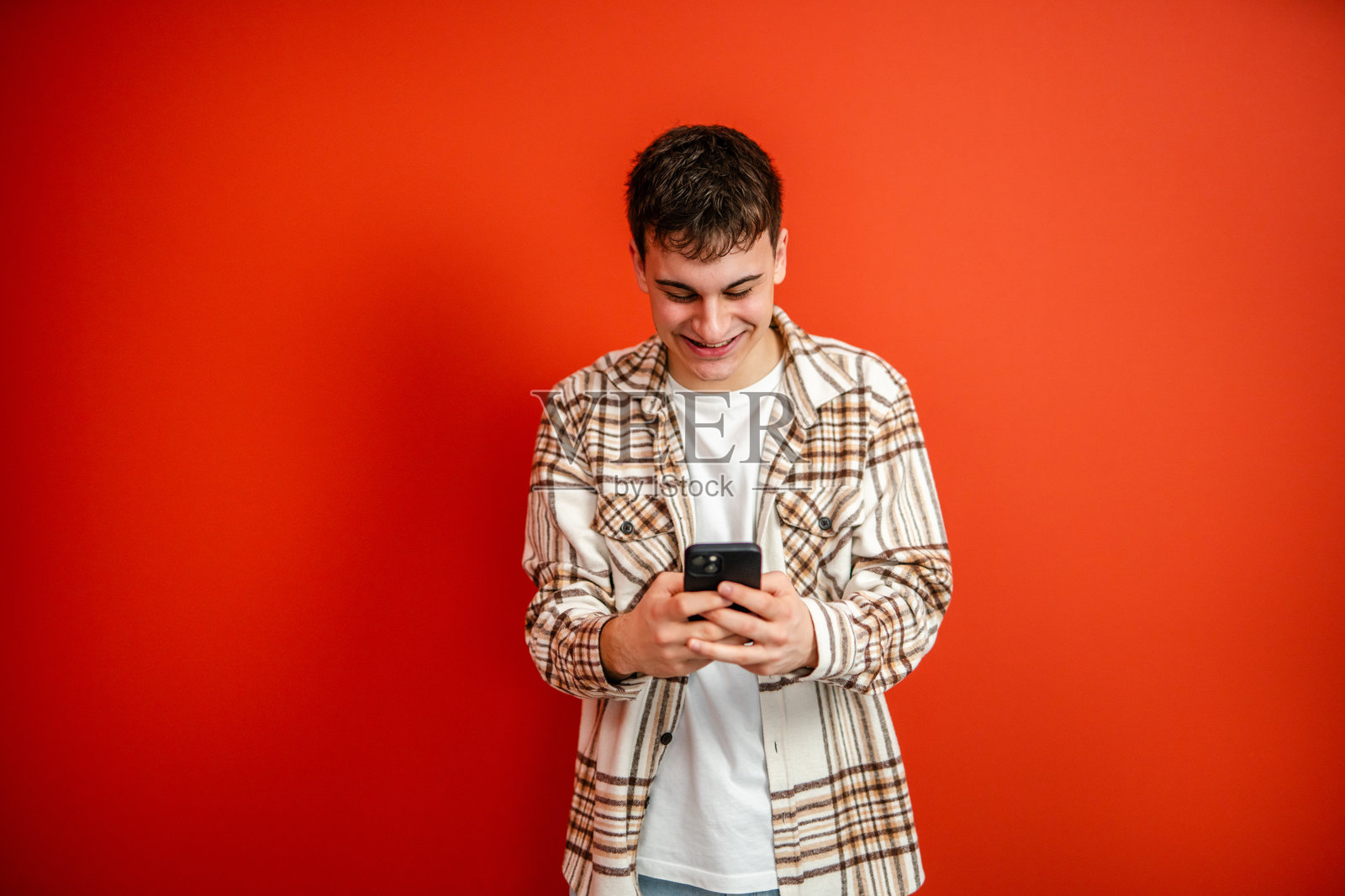 年轻男子在红色背景前使用手机的摄影作品照片摄影图片