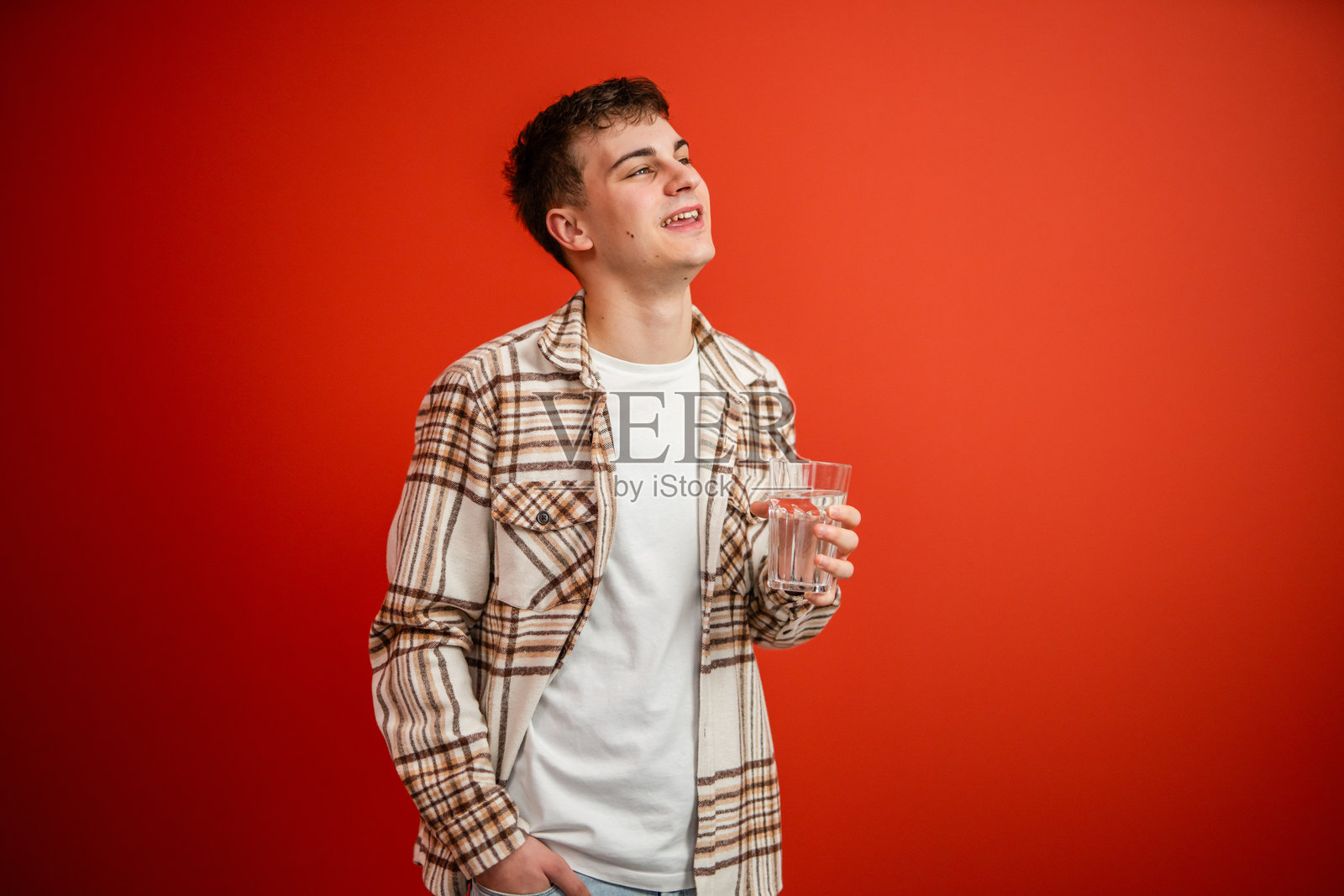 年轻男子在红色背景前喝水的肖像摄影照片摄影图片