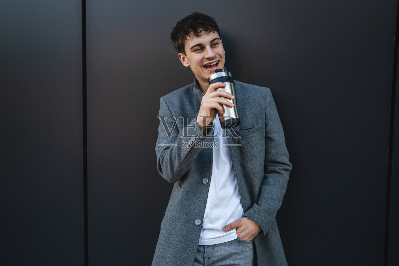 年轻帅气的男人在黑色墙壁背景下喝着保温杯里的咖啡照片摄影图片