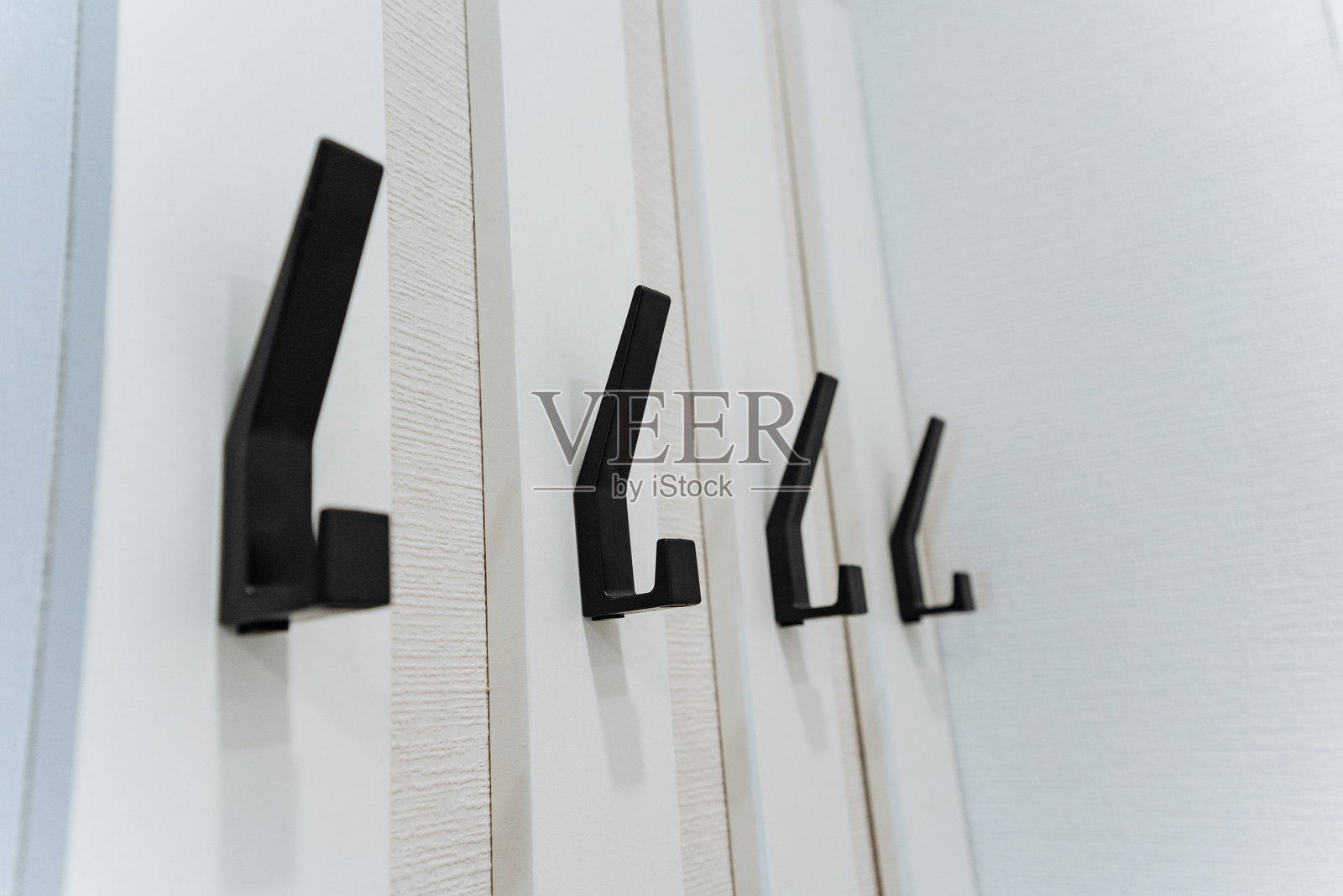 一系列黑色挂钩优雅地悬挂在洁白的墙壁上，与周围环境形成鲜明的视觉对比，吸引人们注意它们独特的设计。照片摄影图片