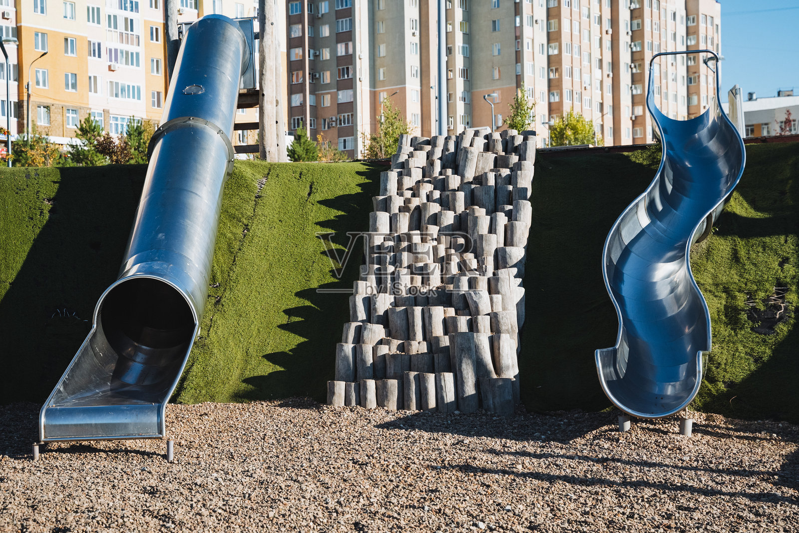 在一个热闹的公园里，有两条闪亮的金属滑梯紧挨着，邀请孩子们和家庭在阳光明媚的日子里来享受乐趣和玩耍。照片摄影图片