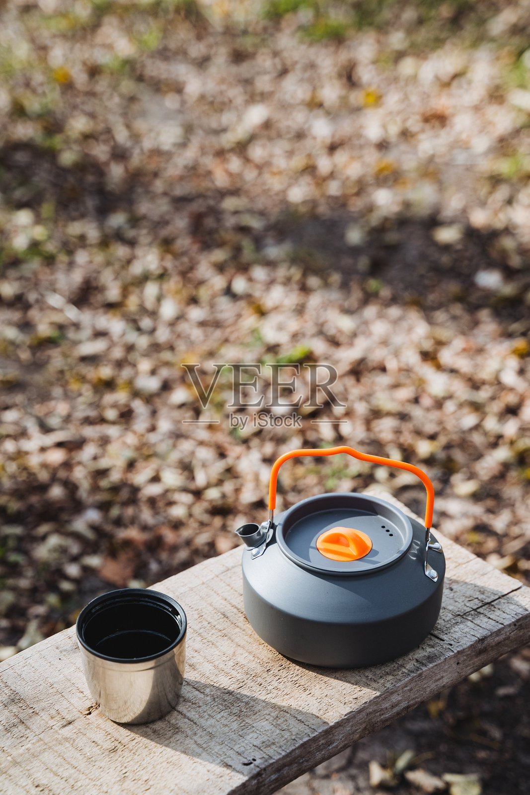 一套便携式露营水壶和杯子静静地放在质朴的木质表面上，完美地环绕在大自然的宁静之中。照片摄影图片