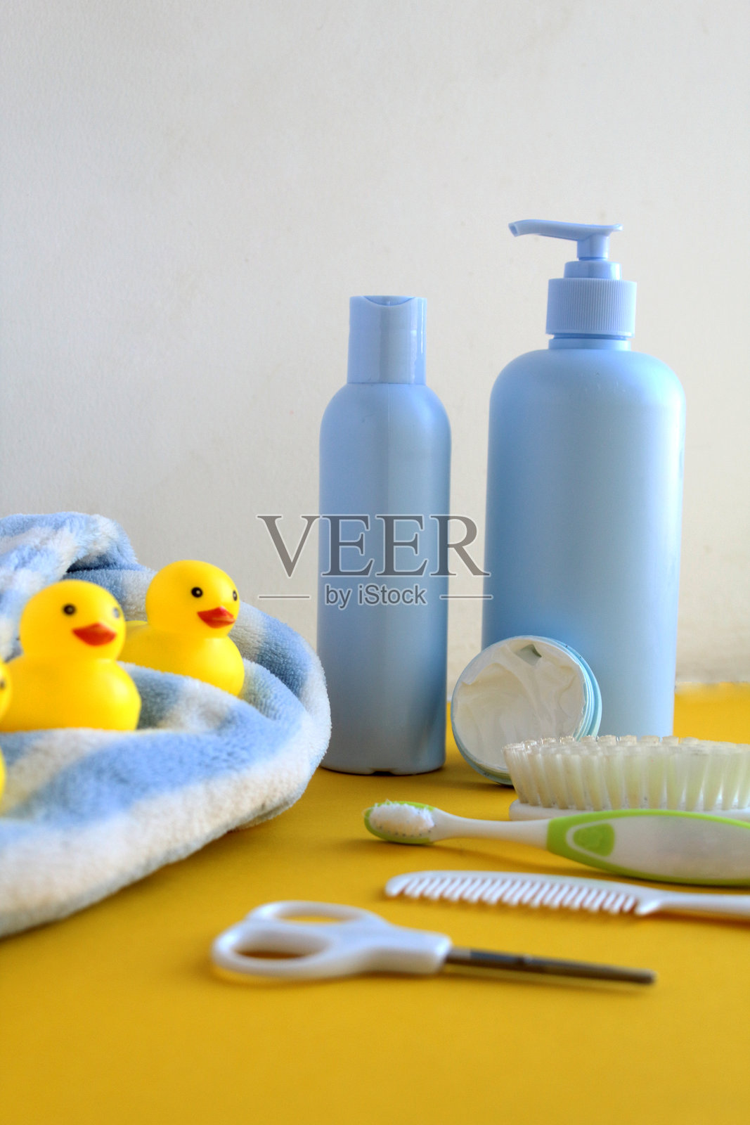 黄色和白色背景上的护肤产品照片。旁边有一只明亮的橡皮鸭。婴儿的蓝白色浴袍。照片摄影图片