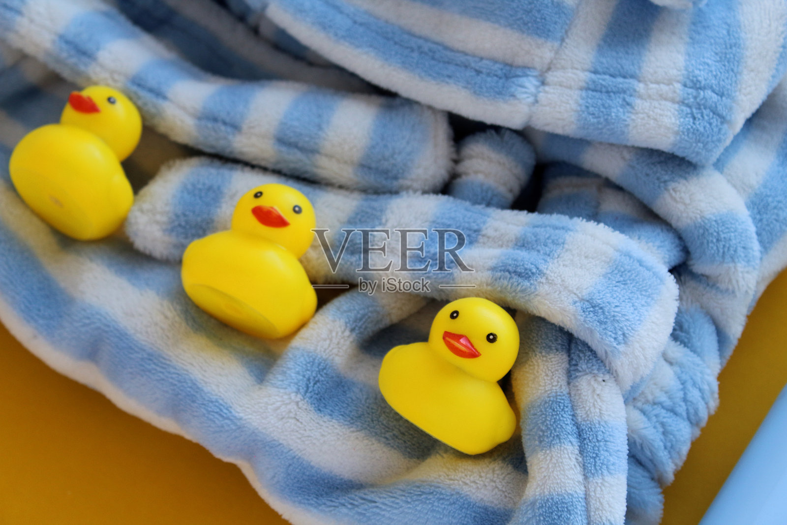 黄色和白色背景上的护肤产品照片。旁边有一只明亮的橡皮鸭。婴儿的蓝白色浴袍。照片摄影图片