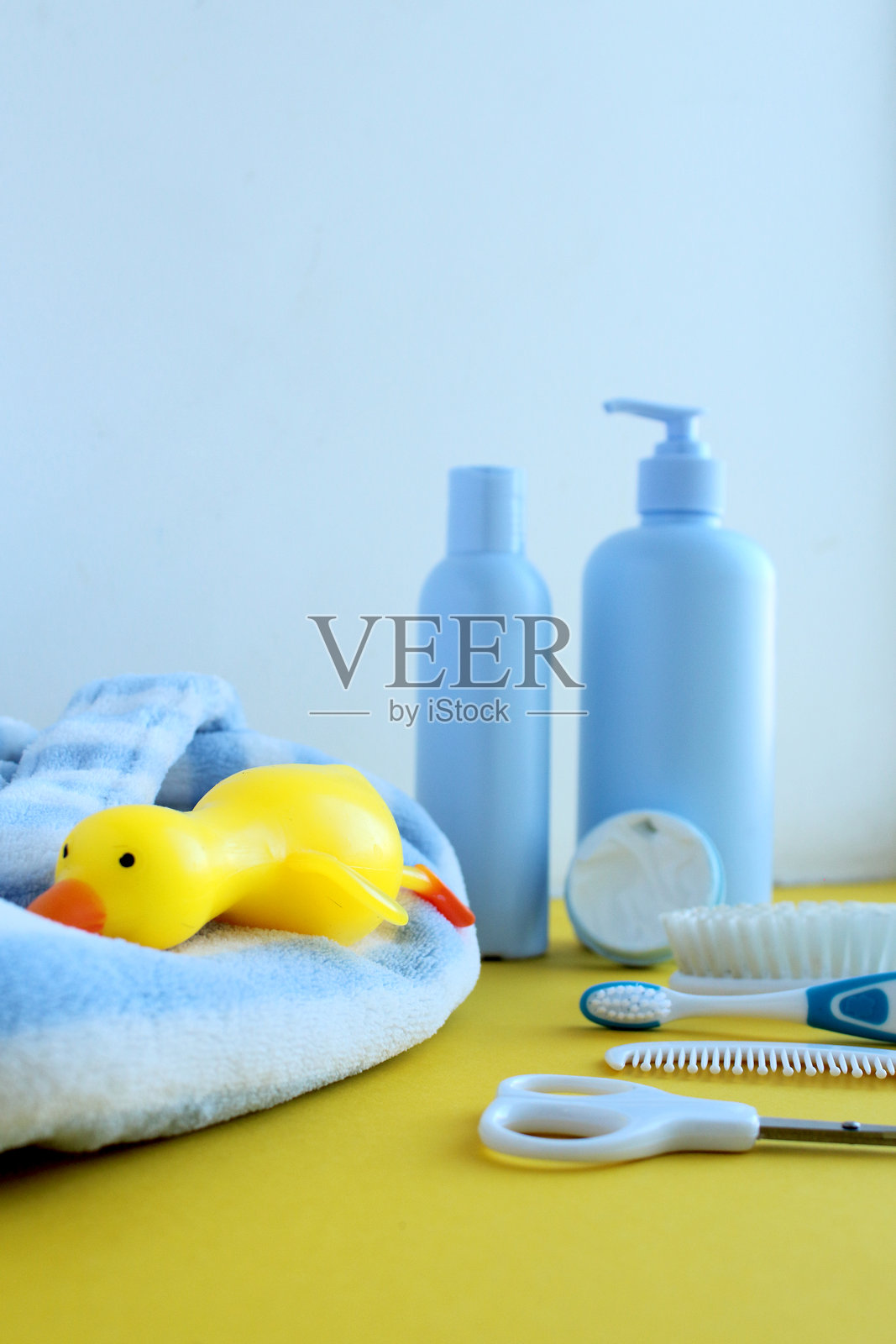 黄色和白色背景上的护肤产品照片。旁边有一只明亮的橡皮鸭。婴儿的蓝白色浴袍。照片摄影图片