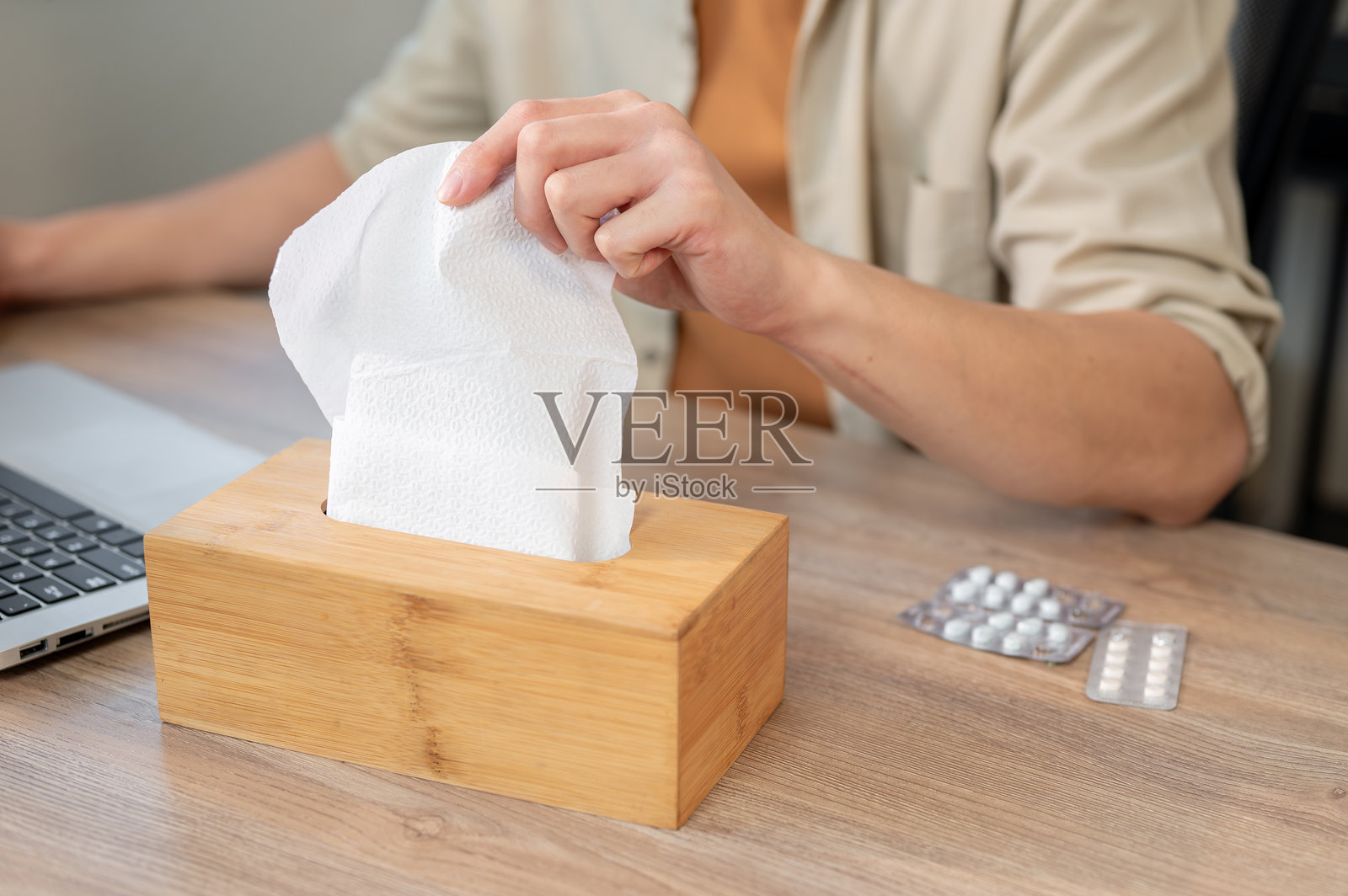 一名男子在办公室的桌子上工作时，伸手从纸巾盒中拿纸巾的特写镜头。照片摄影图片