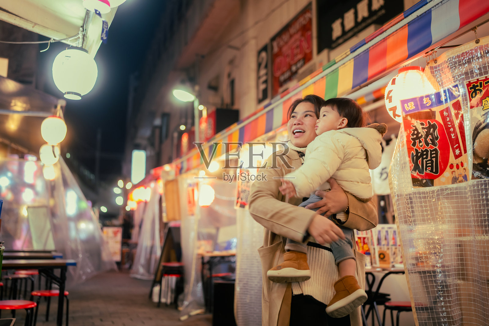 年轻的亚洲母亲在日本旅行生活中，夜晚拥抱可爱的小儿子，享受美丽的城市街道。照片摄影图片