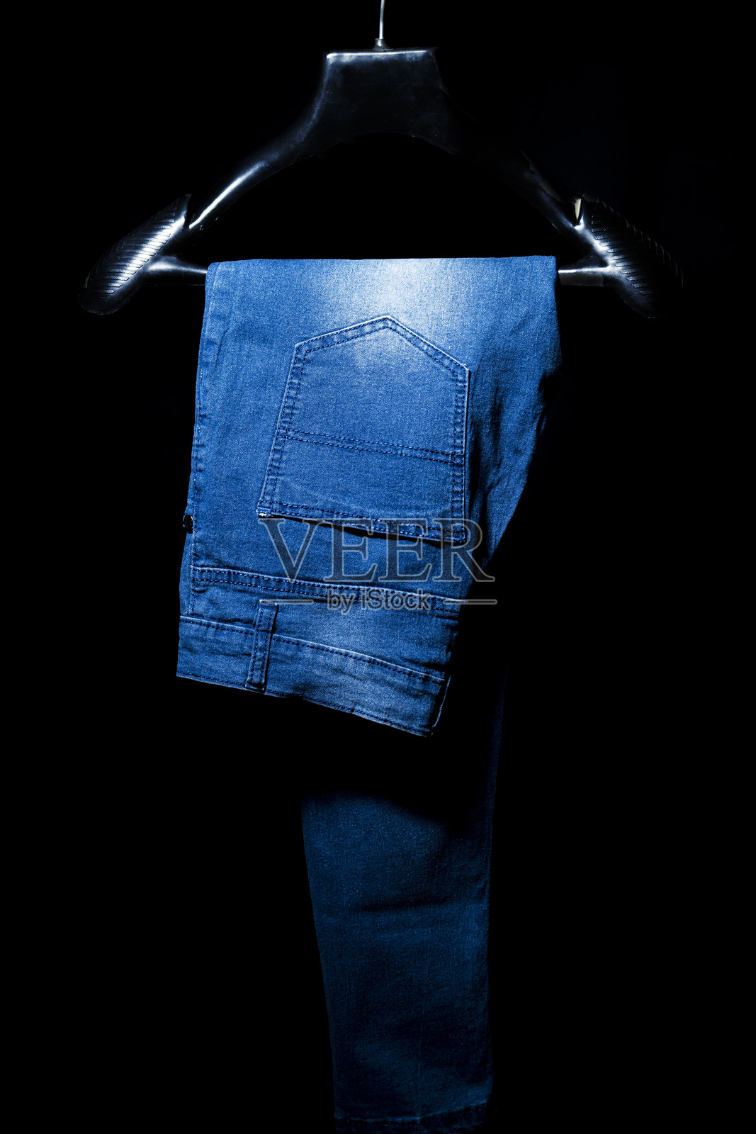 黑色背景上的蓝色牛仔裤挂在衣架上照片摄影图片