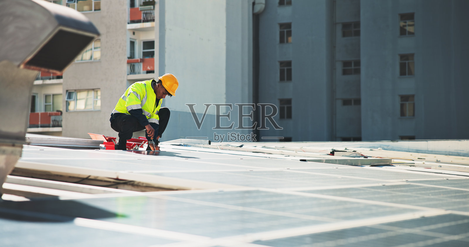 城市中有一名男子在屋顶上修理太阳能电池板，涉及光伏电网、技术员和工程师。可再生能源、发电机和电力系统，适合承包商和维护人员。照片摄影图片