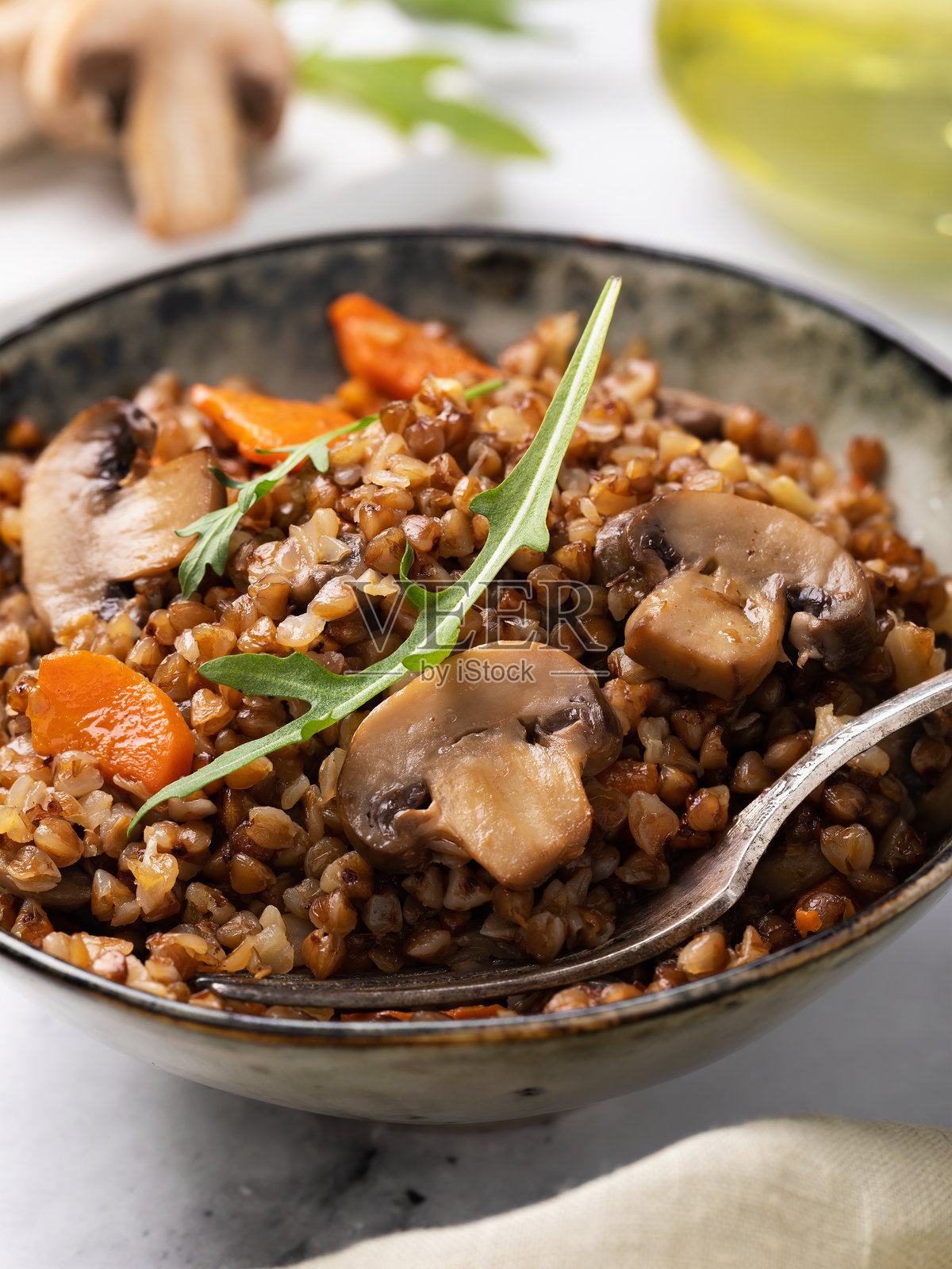 桌子上的陶瓷盘中盛着荞麦粥，配有蘑菇、胡萝卜和生菜叶，特写镜头。照片摄影图片