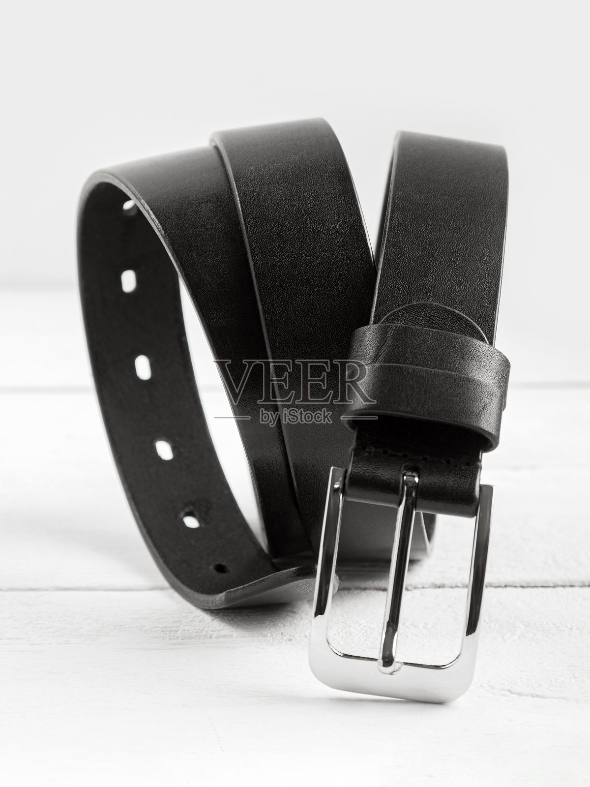 黑色真皮皮带放在白色木质背景上。照片摄影图片