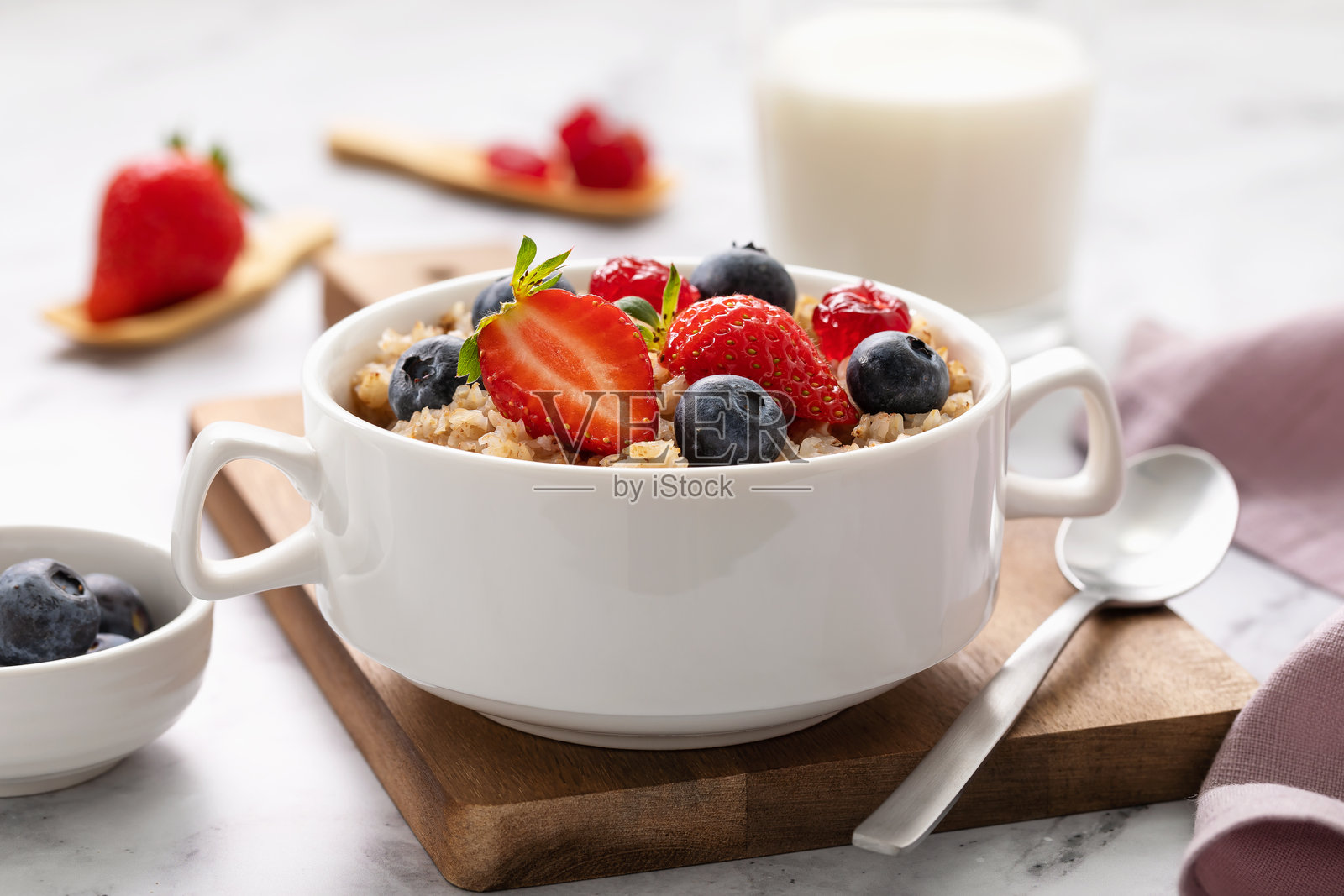 白色陶瓷盘中的荞麦片，搭配草莓、蓝莓和干樱桃，放在木托盘上，早餐粥。照片摄影图片