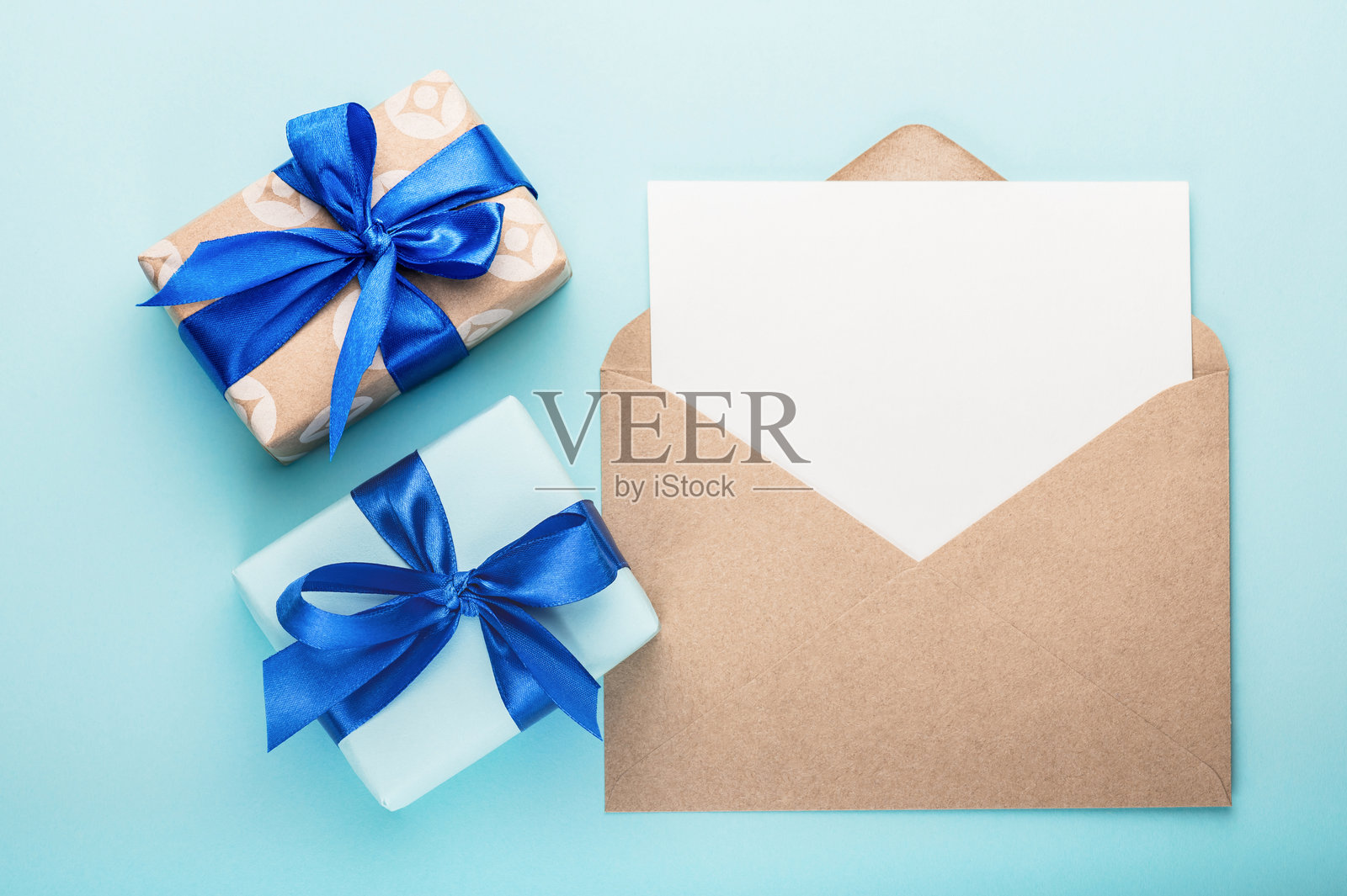 两个带蓝色丝带和蝴蝶结的礼品盒，以及一个空白贺卡和信封，背景为蓝色。贺卡。照片摄影图片