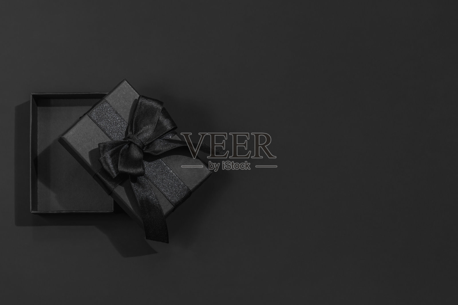 黑色礼品盒打开，缎带系成蝴蝶结，背景为深黑色，留有文字空间。照片摄影图片