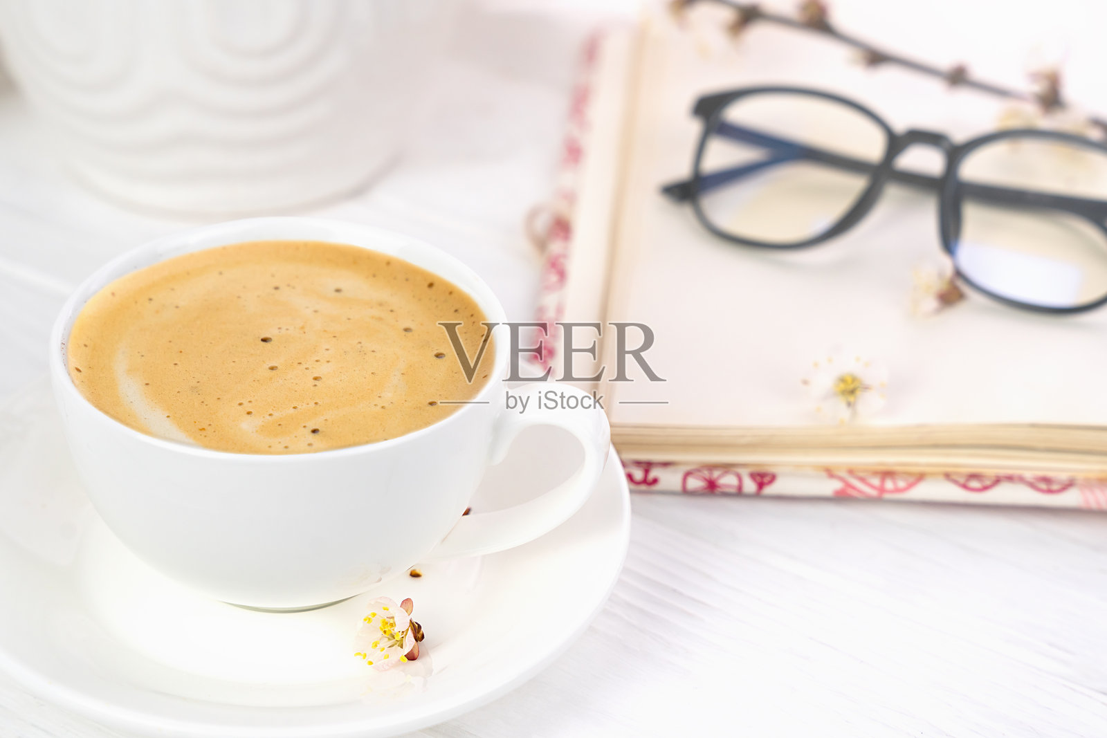 一杯新鲜的早晨卡布奇诺、笔记本和眼镜放在桌子上。早晨的放松。春天的心情。选择性焦点。照片摄影图片