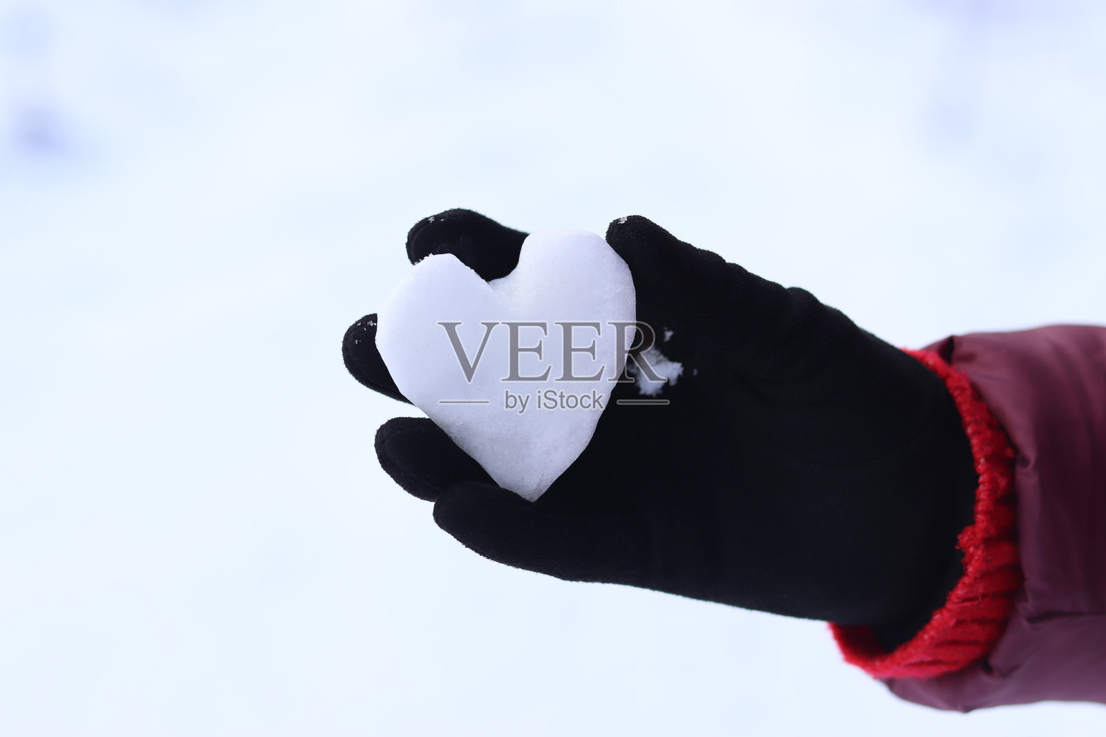 女性手戴着黑色冬季手套，手中捧着雪，形成一个心形。照片摄影图片