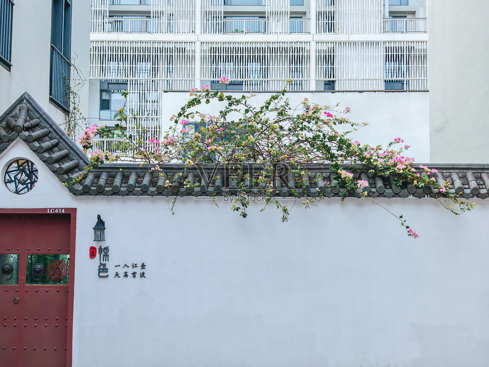 中国，深圳上坡。传统的白墙，红门，粉色花朵，背景是现代购物中心建筑。照片摄影图片