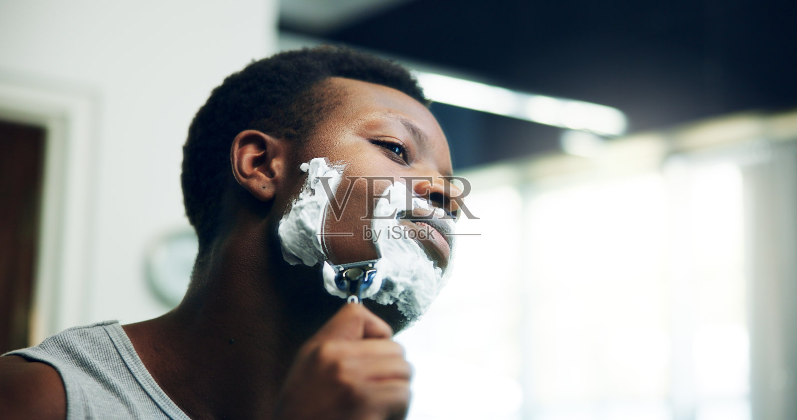 黑人男性在家浴室中使用剃刀和面霜进行修饰、脱毛或剃须。非洲男性或面部使用刀片，剃须后使用面霜或清洁胡须的护肤程序。照片摄影图片