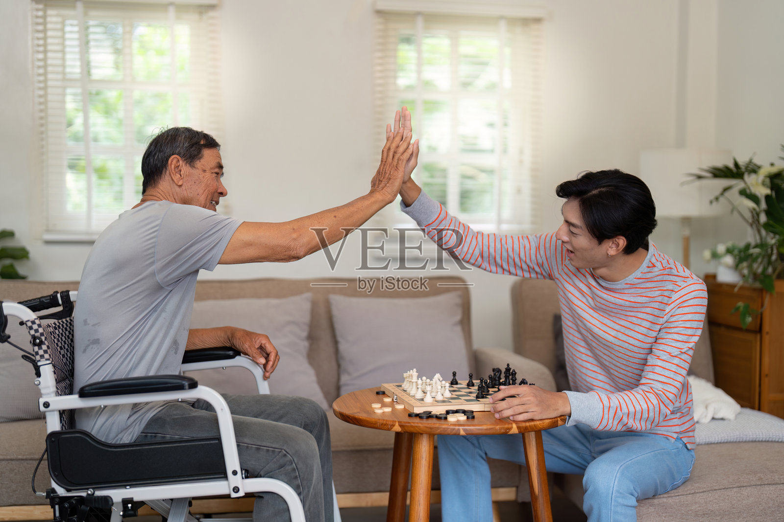 父子在温馨的客厅里庆祝棋局的一步，击掌庆祝，强调家庭的快乐与联系。照片摄影图片