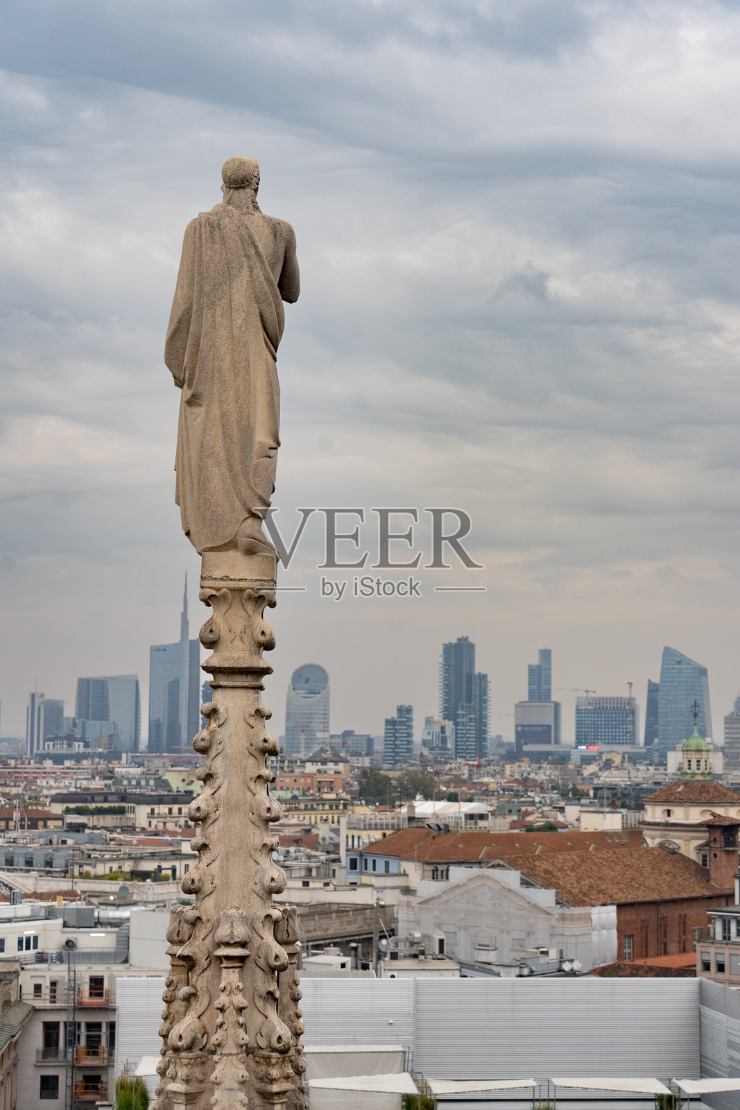 米兰大教堂屋顶上的雕像俯瞰着城市，远眺现代建筑的天际线。照片摄影图片