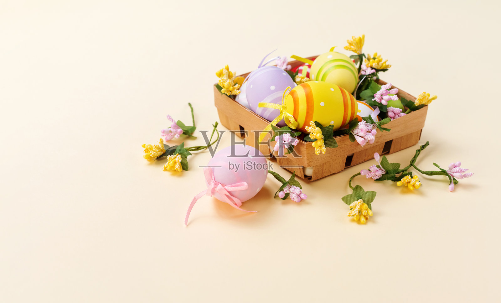 复活节篮子里装满了装饰彩蛋。方形篮子里有彩绘的鸡蛋和花朵，背景是柔和的黄色。俯视图。照片摄影图片