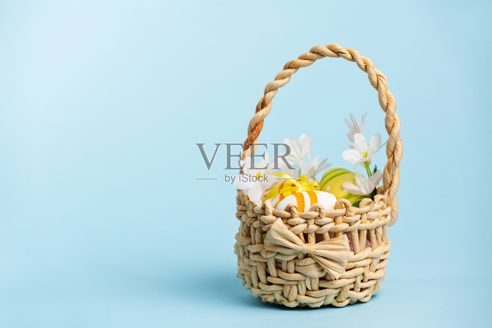 复活节篮子里装满了装饰彩蛋。白色柳条篮子里有彩绘的鸡蛋和花朵，背景是柔和的蓝色。照片摄影图片