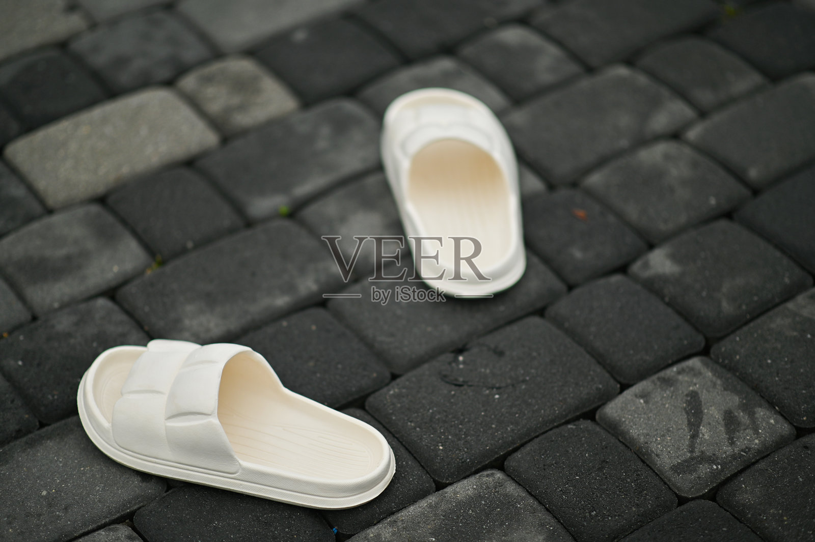 一双白色拖鞋放在灰色湿润的铺路石上照片摄影图片