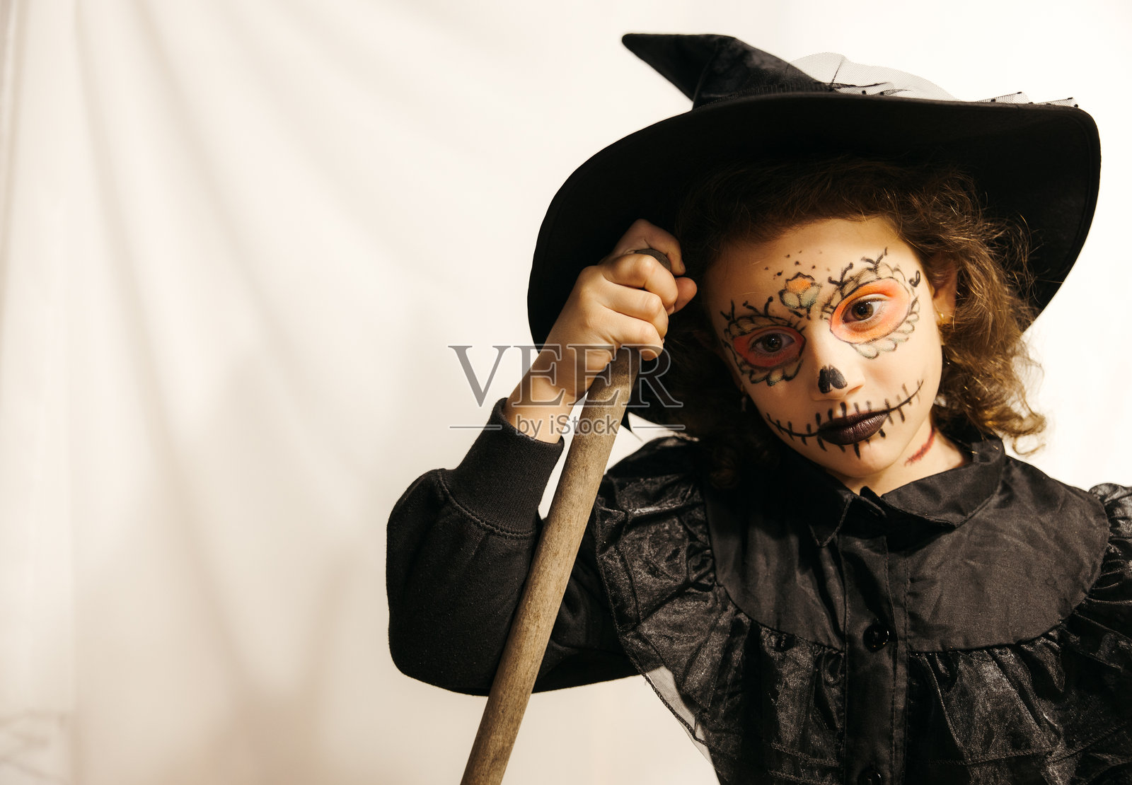 思考中的女孩穿着女巫服装，脸上涂有彩妆，手持扫帚，留有空白空间。照片摄影图片
