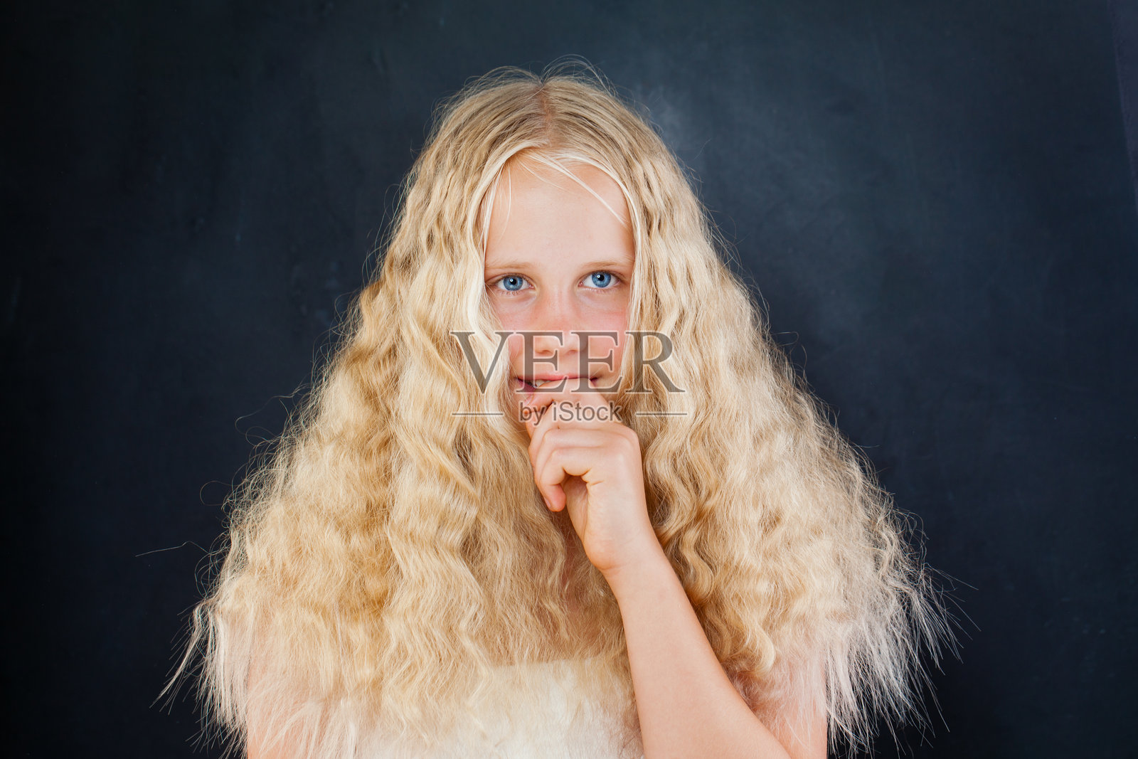 思考的孩子，金色长波浪发，注视着黑色背景下的镜头，时尚肖像照片摄影图片