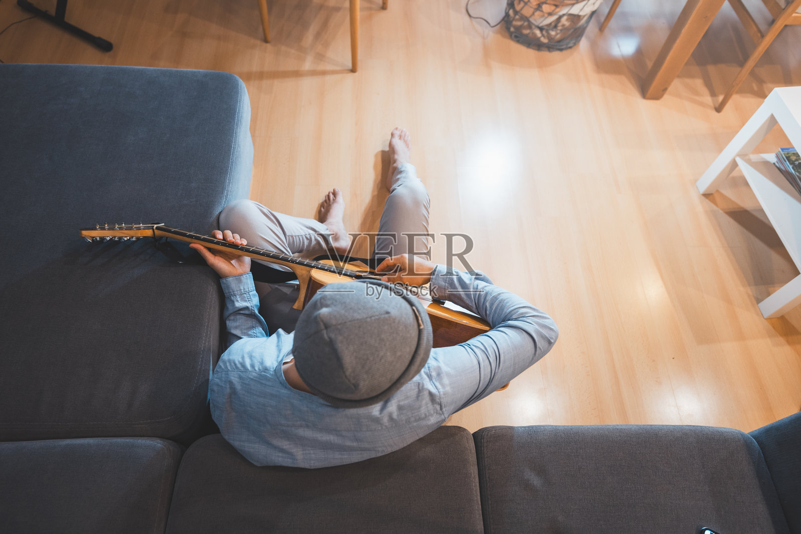 音乐家坐在灰色沙发上，随意拨动着一把木吉他，沉浸在放松和内省的时刻，营造出宁静而富有创意的氛围。俯视图照片摄影图片