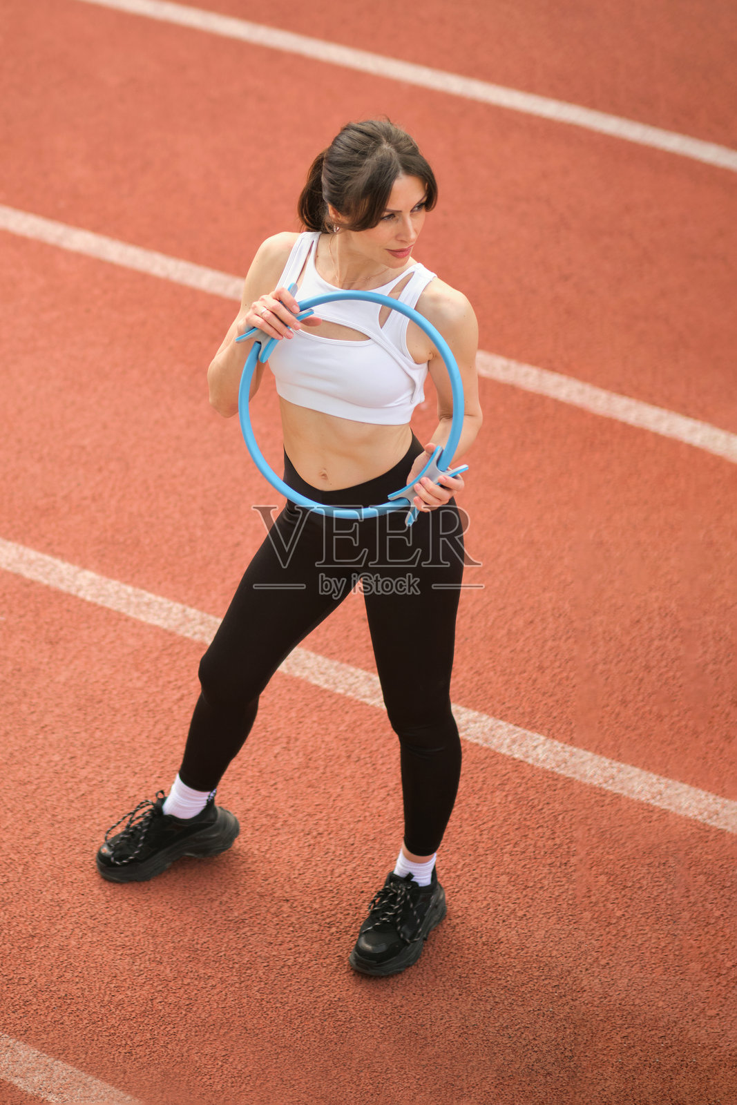 一位健康的女性在跑道上将普拉提环举过头顶，坚定的表情彰显了她的专注。这张图片展示了使用健身工具来增强锻炼效果。照片摄影图片