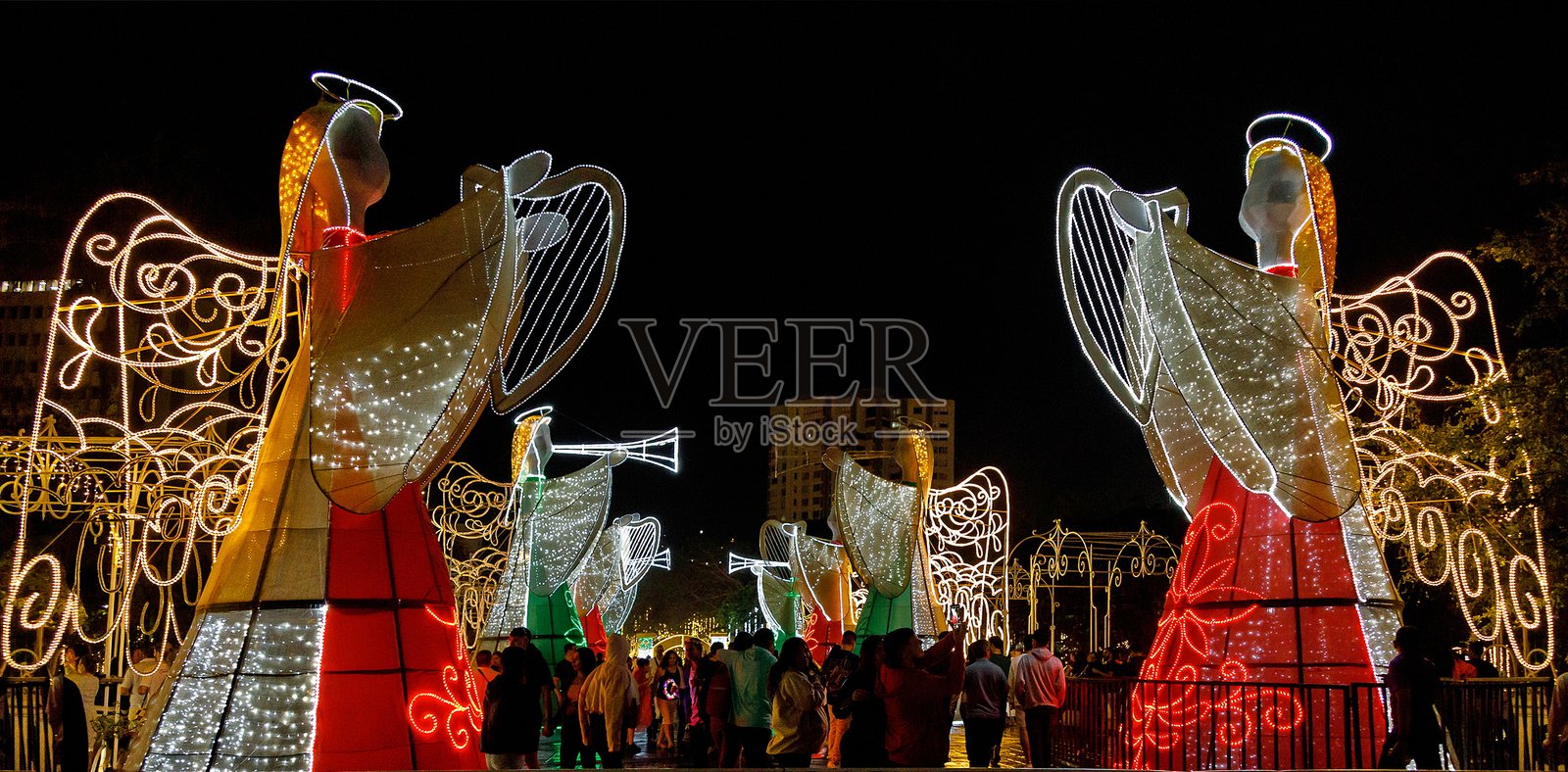 人们在哥伦比亚瓦耶尔德卡卡的主广场中，走过大型发光天使，作为节日灯光展示的一部分。照片摄影图片