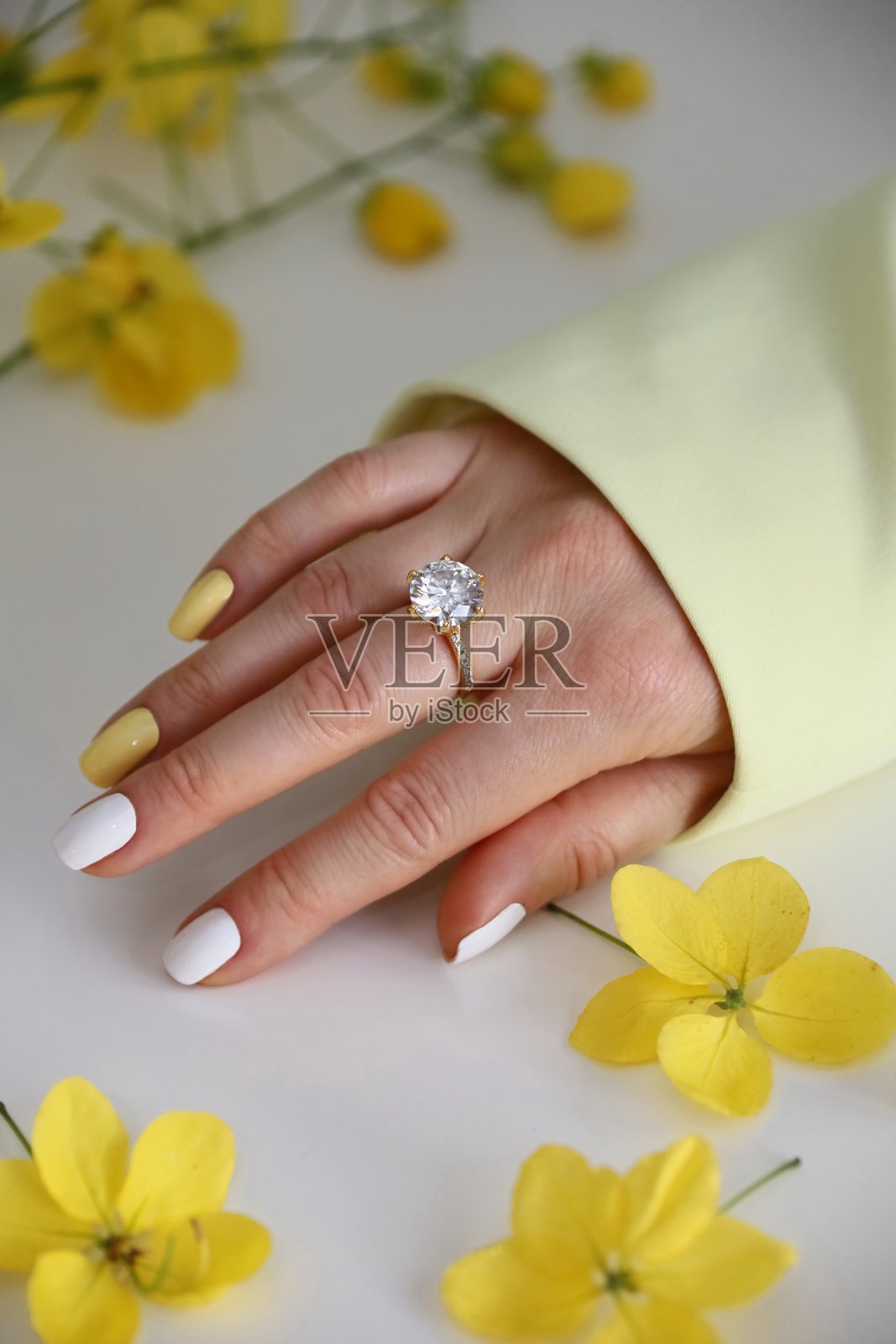 女人手上戴着清澈宝石的订婚戒指，手周围环绕着黄色花朵的设计照片摄影图片